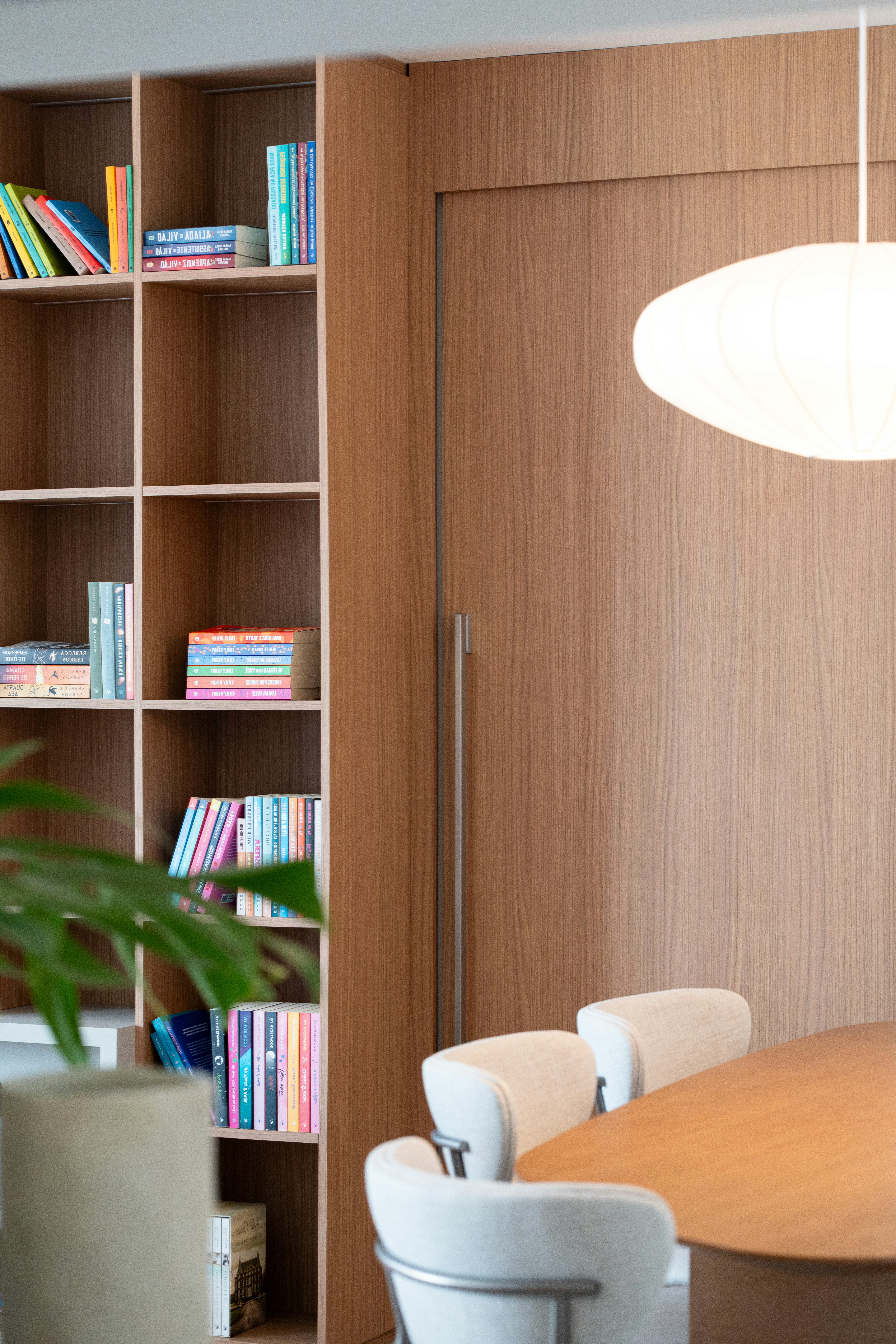 Modern living space with wooden bookshelf, dining table, and chairs.