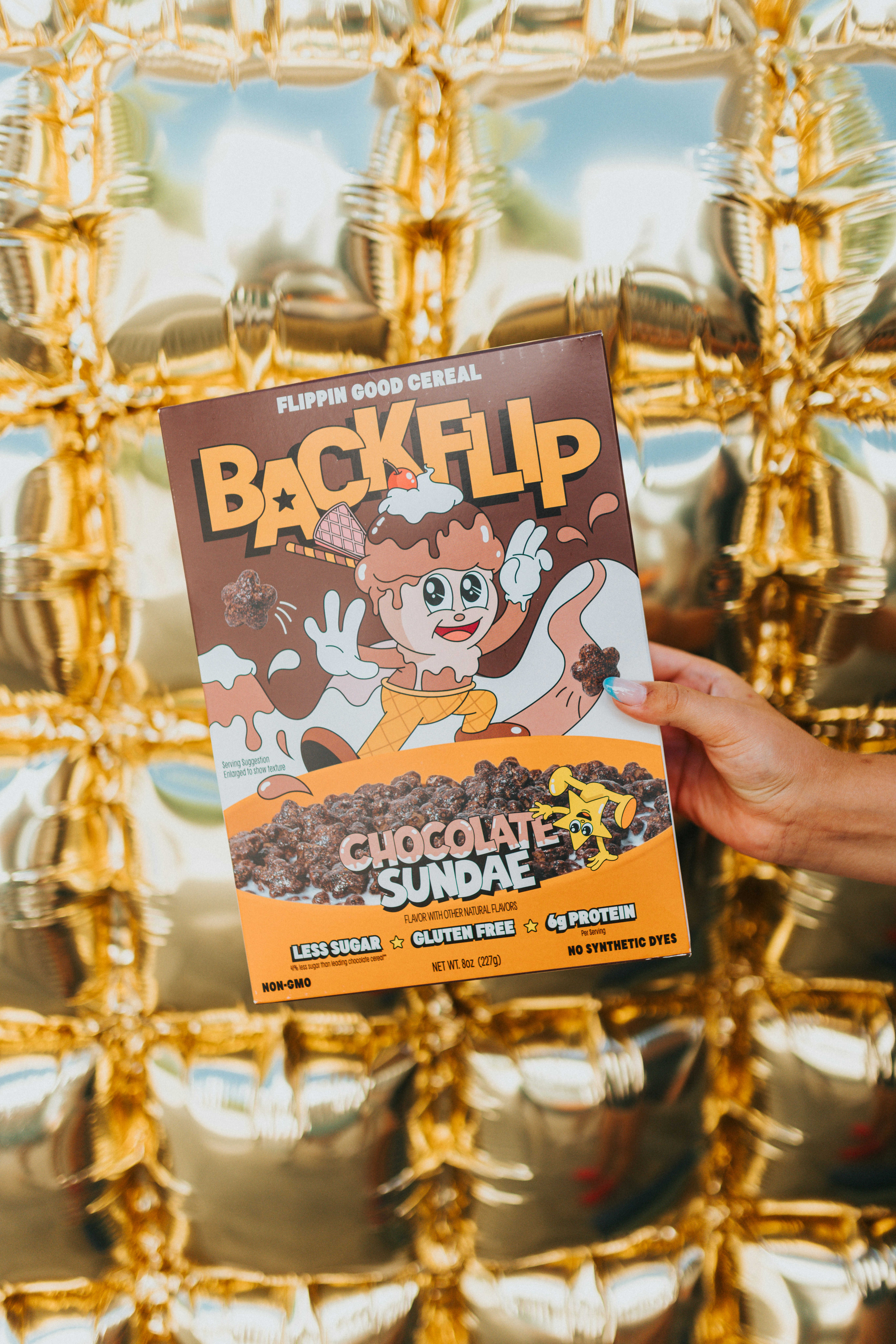 Hand holding backflip chocolate sundae cereal against golden background.
