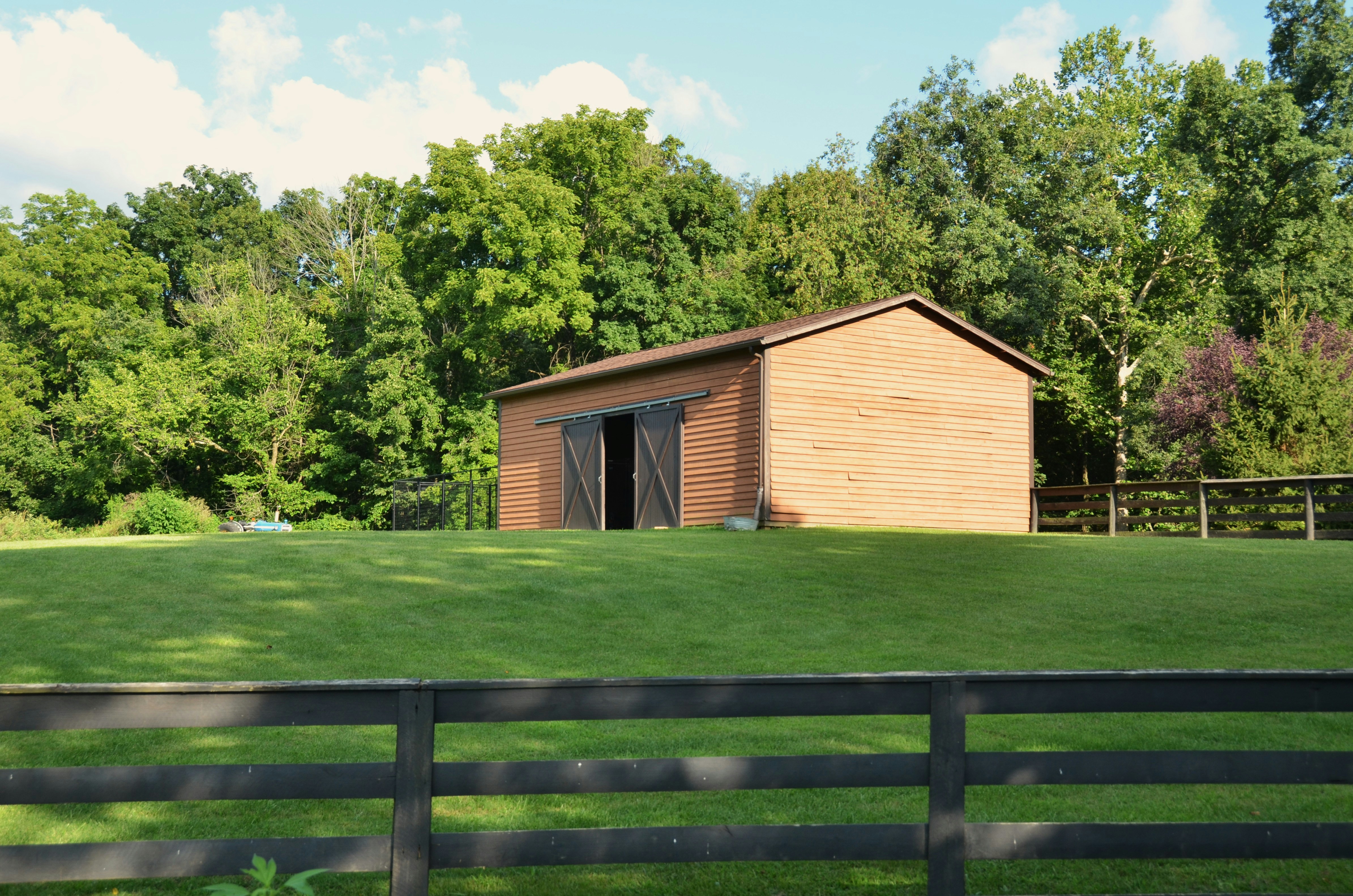 A small brown barn in a grassy field with trees.