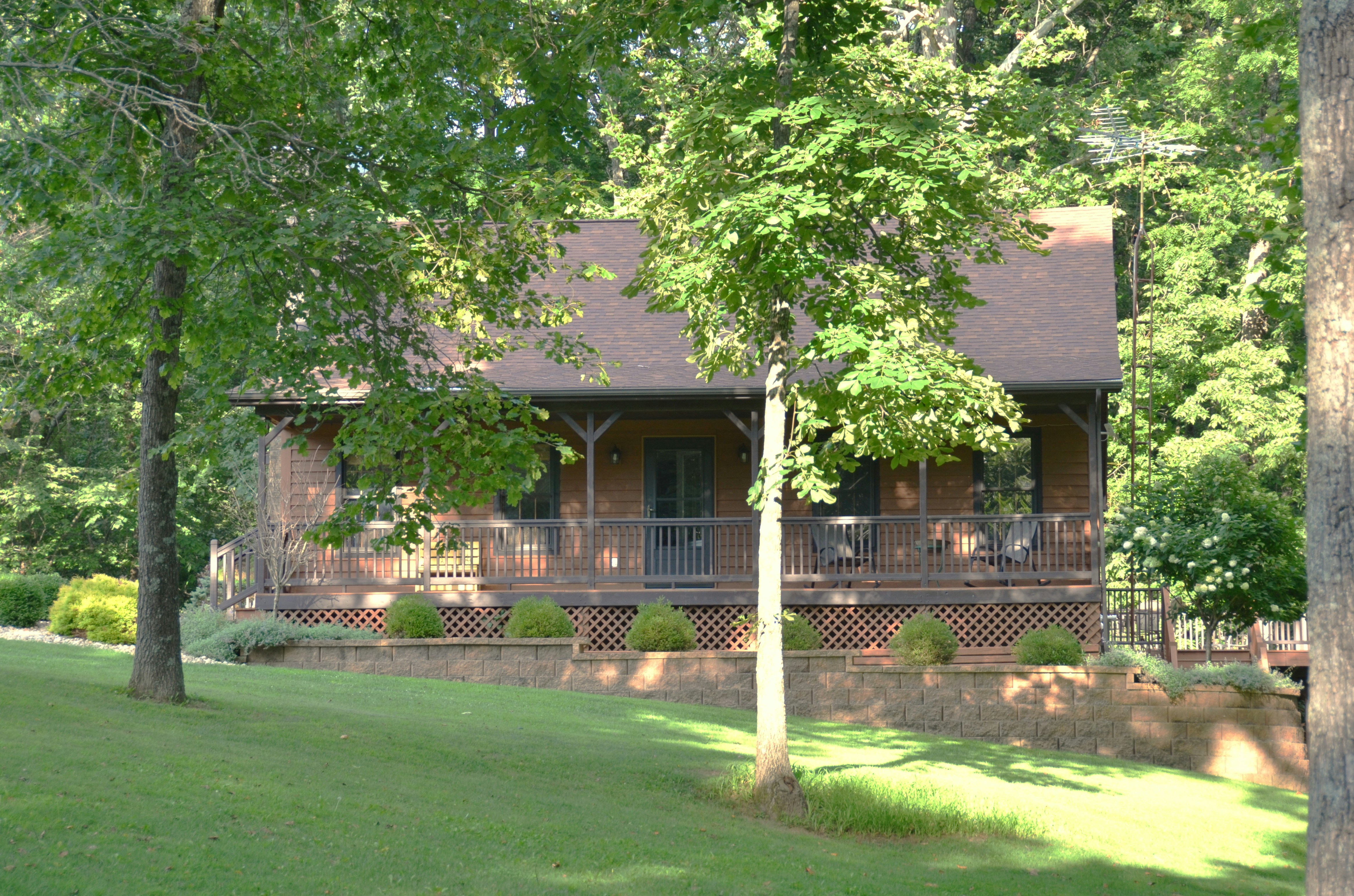 Rustic cabin with a porch surrounded by lush green trees.