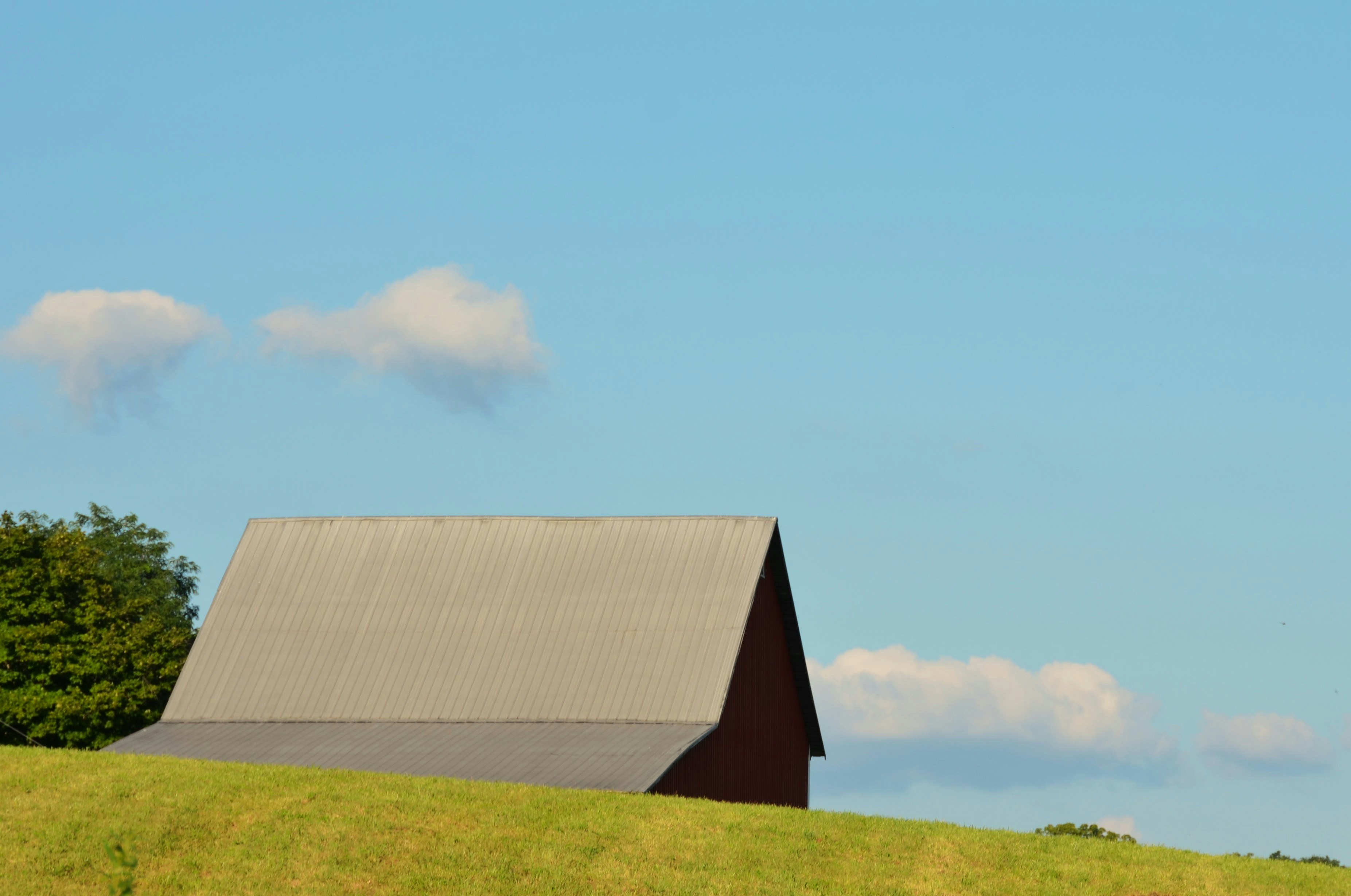 Barn on a green hill with blue sky.