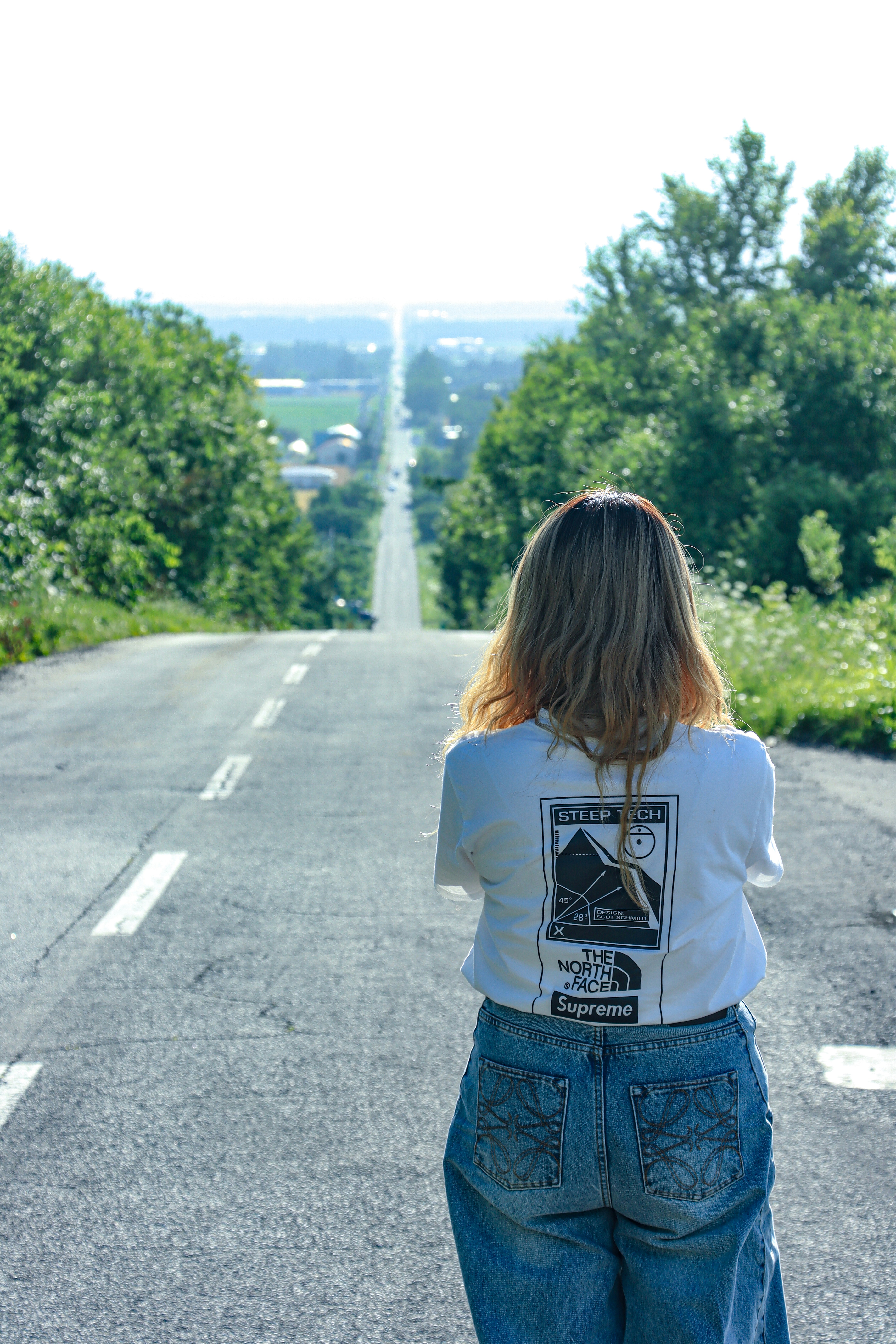 A person looks down a long, straight road with trees