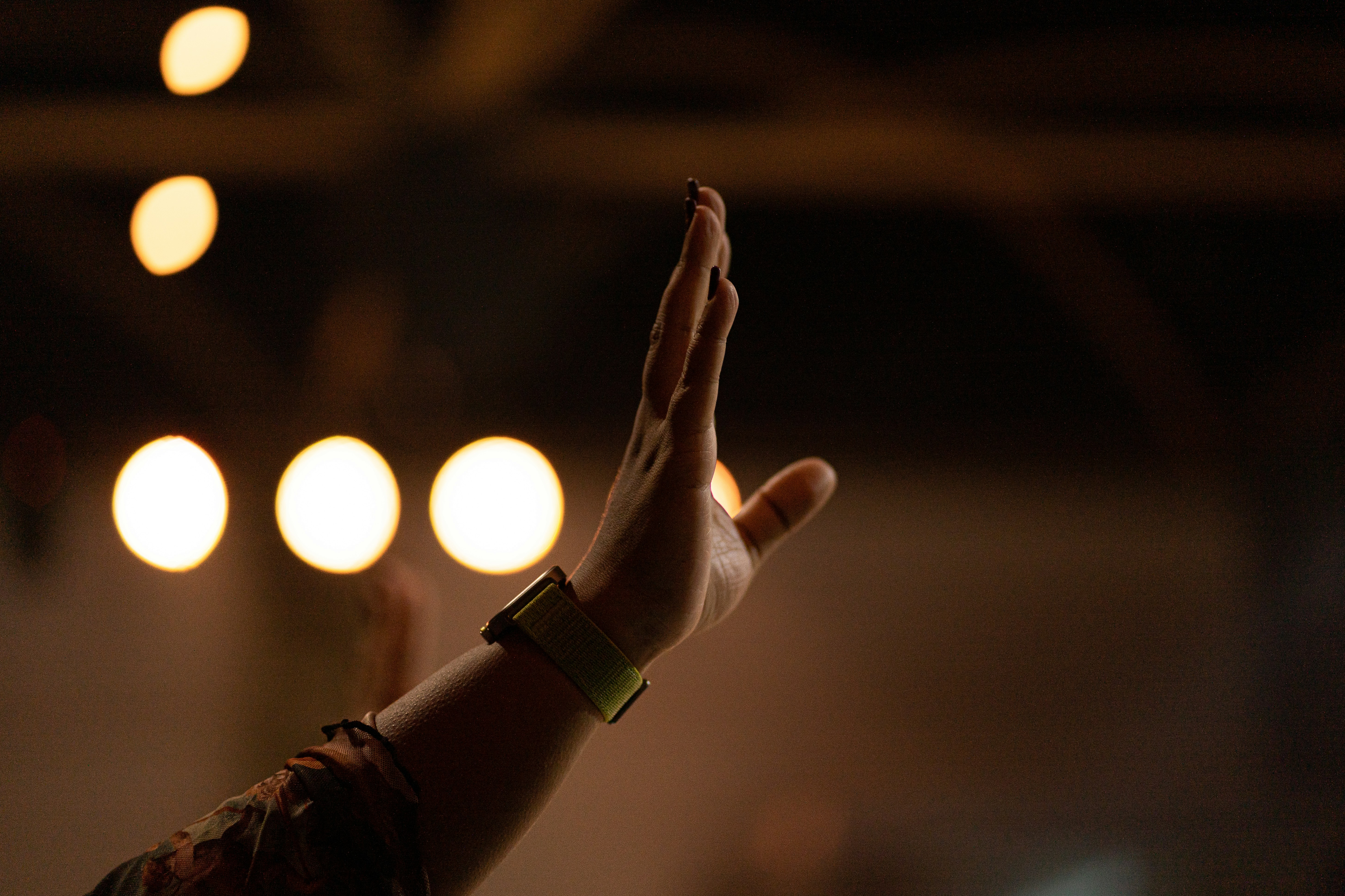 Hand raised in praise with warm bokeh lights