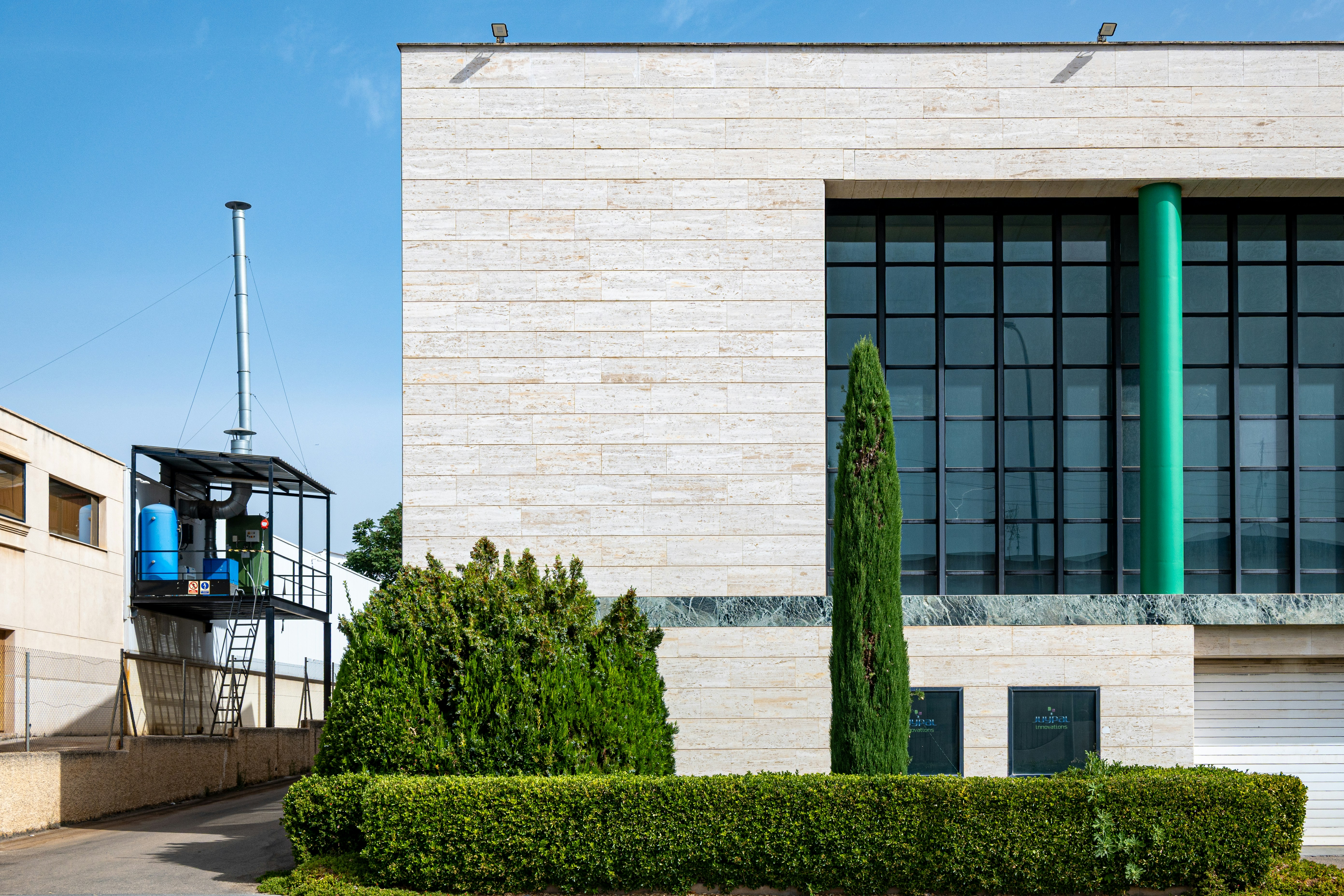 Modern building, green column, cypress tree, and industrial structure.