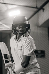 A cricketer wearing a helmet and holding a bat indoors.
