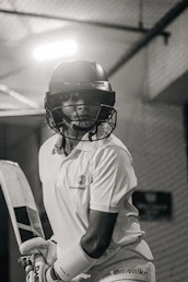A cricketer wearing a helmet and holding a bat indoors.