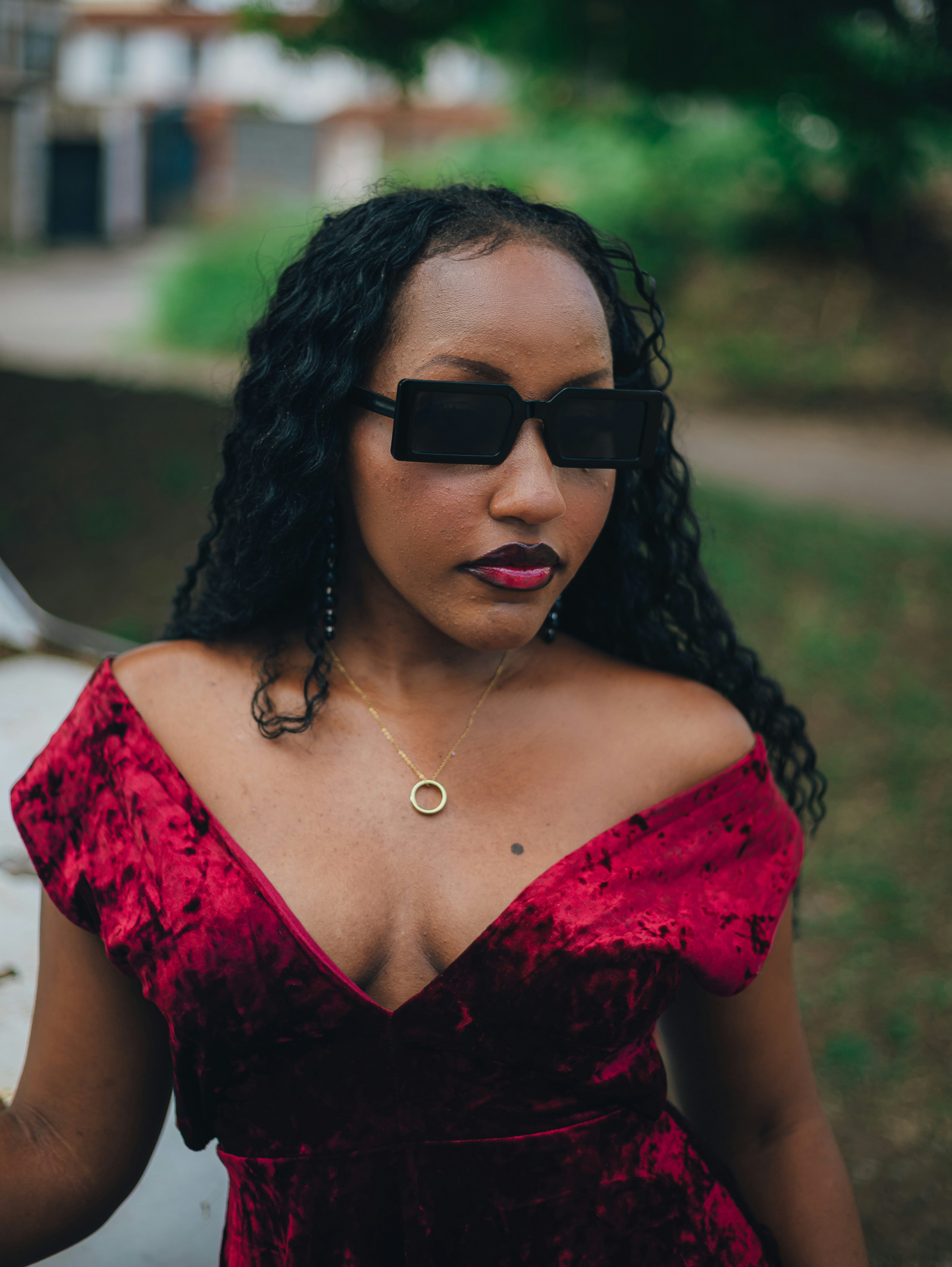A stylish woman wearing a red velvet dress and sunglasses.