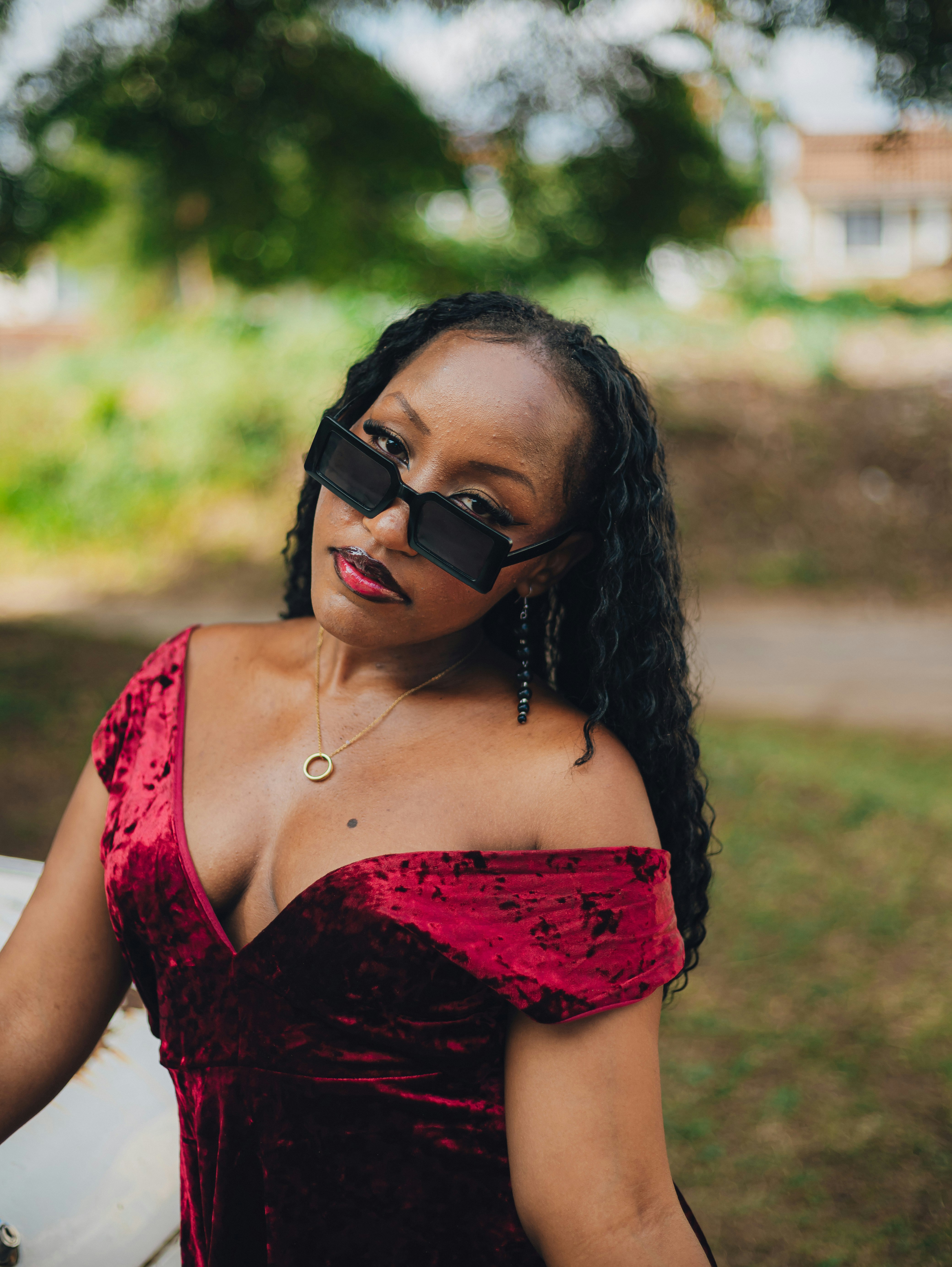 A woman in a red velvet dress and stylish sunglasses.
