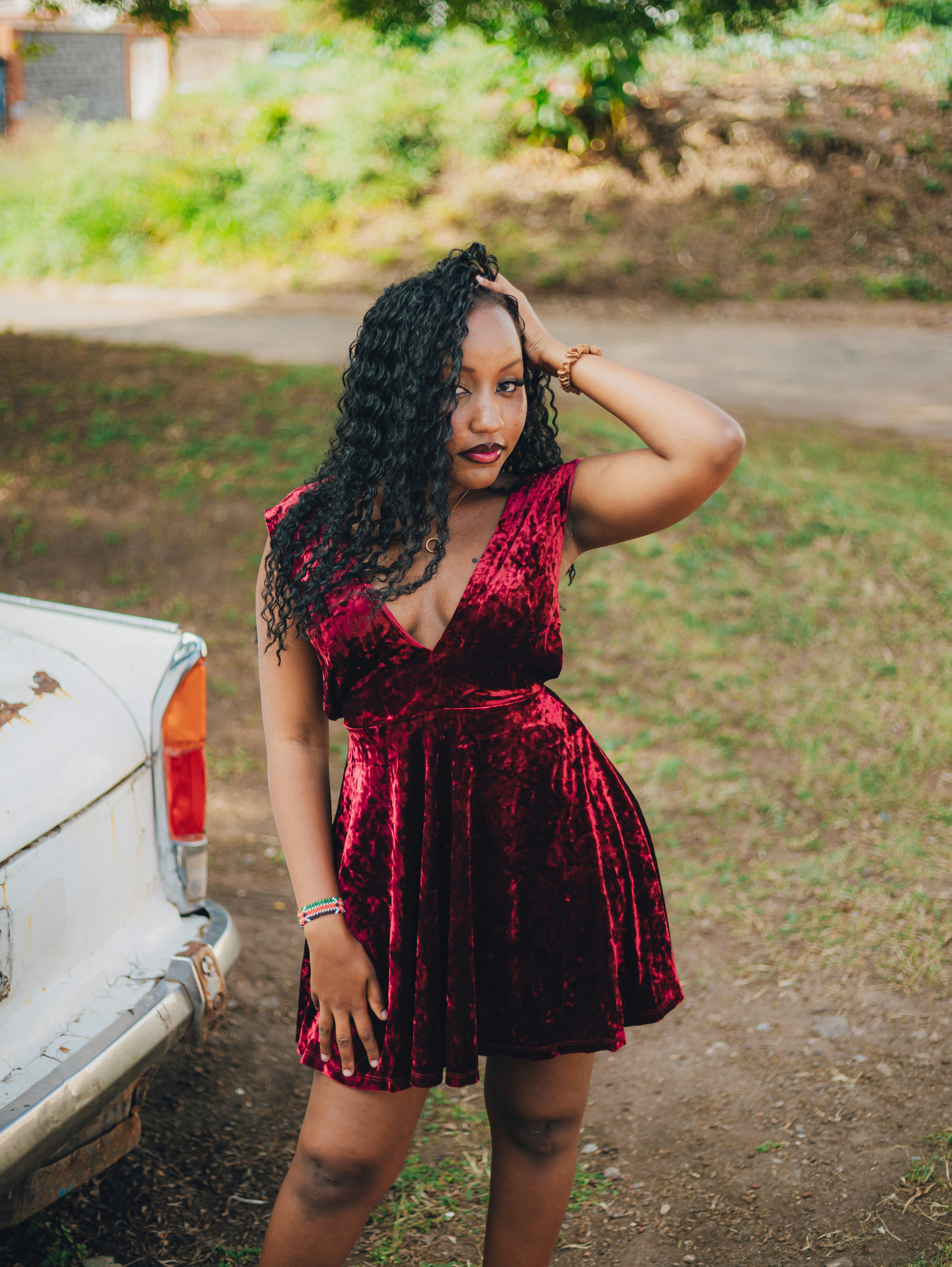 Young woman poses in a red velvet dress outdoors.