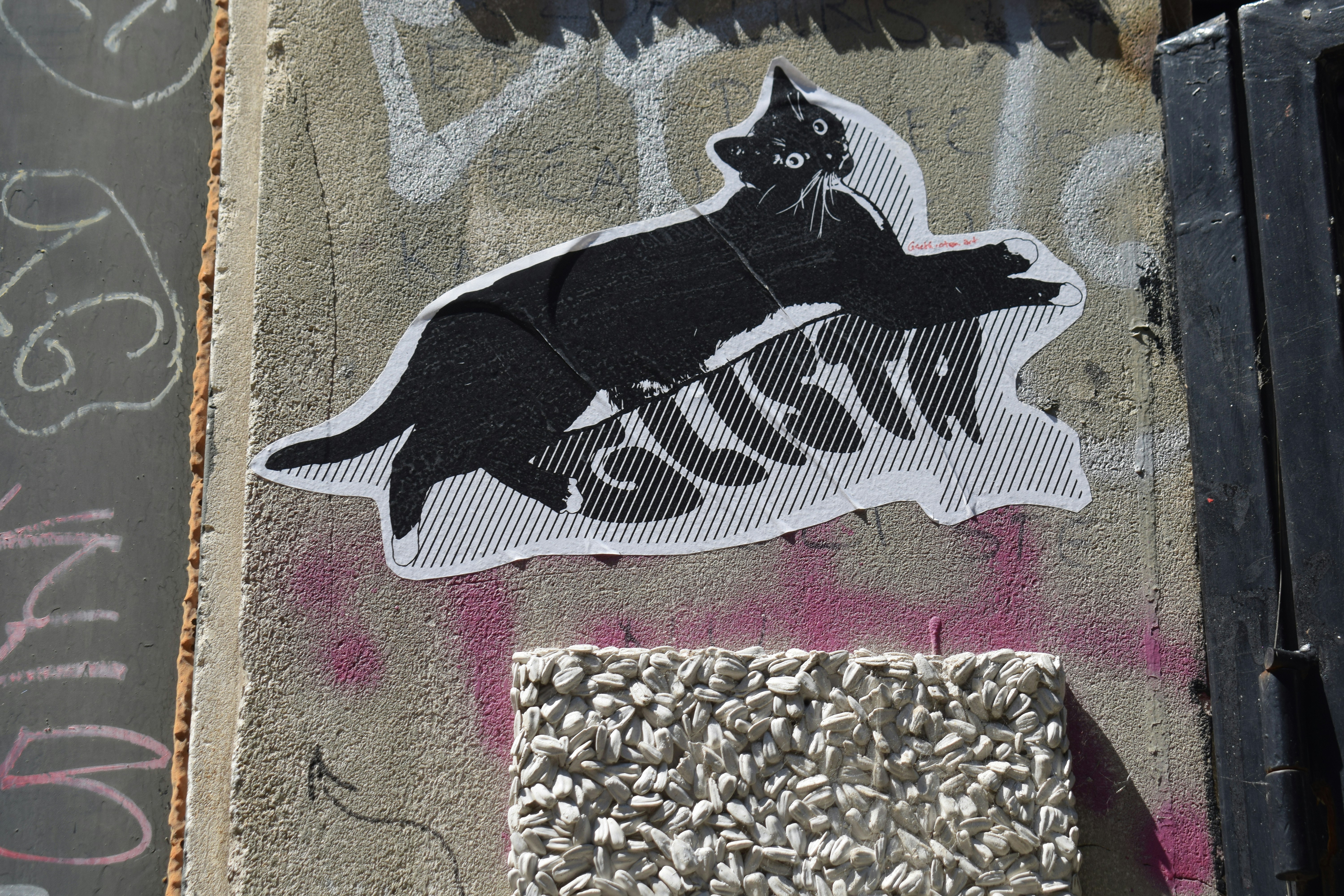 A black cat sticker with "gusta" on a concrete wall