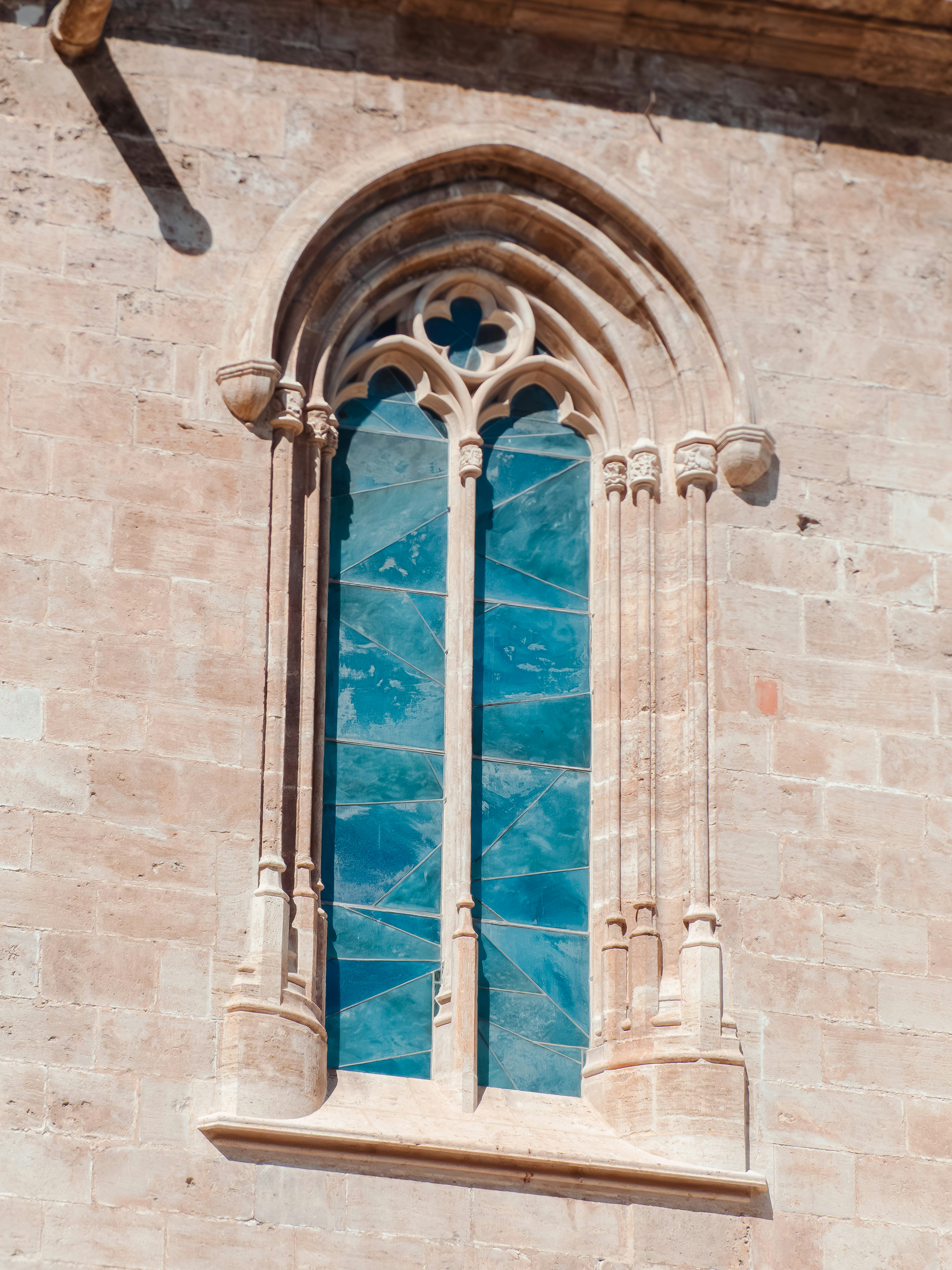 Fotomural Ancient gothic window with blue stained glass in stone wall