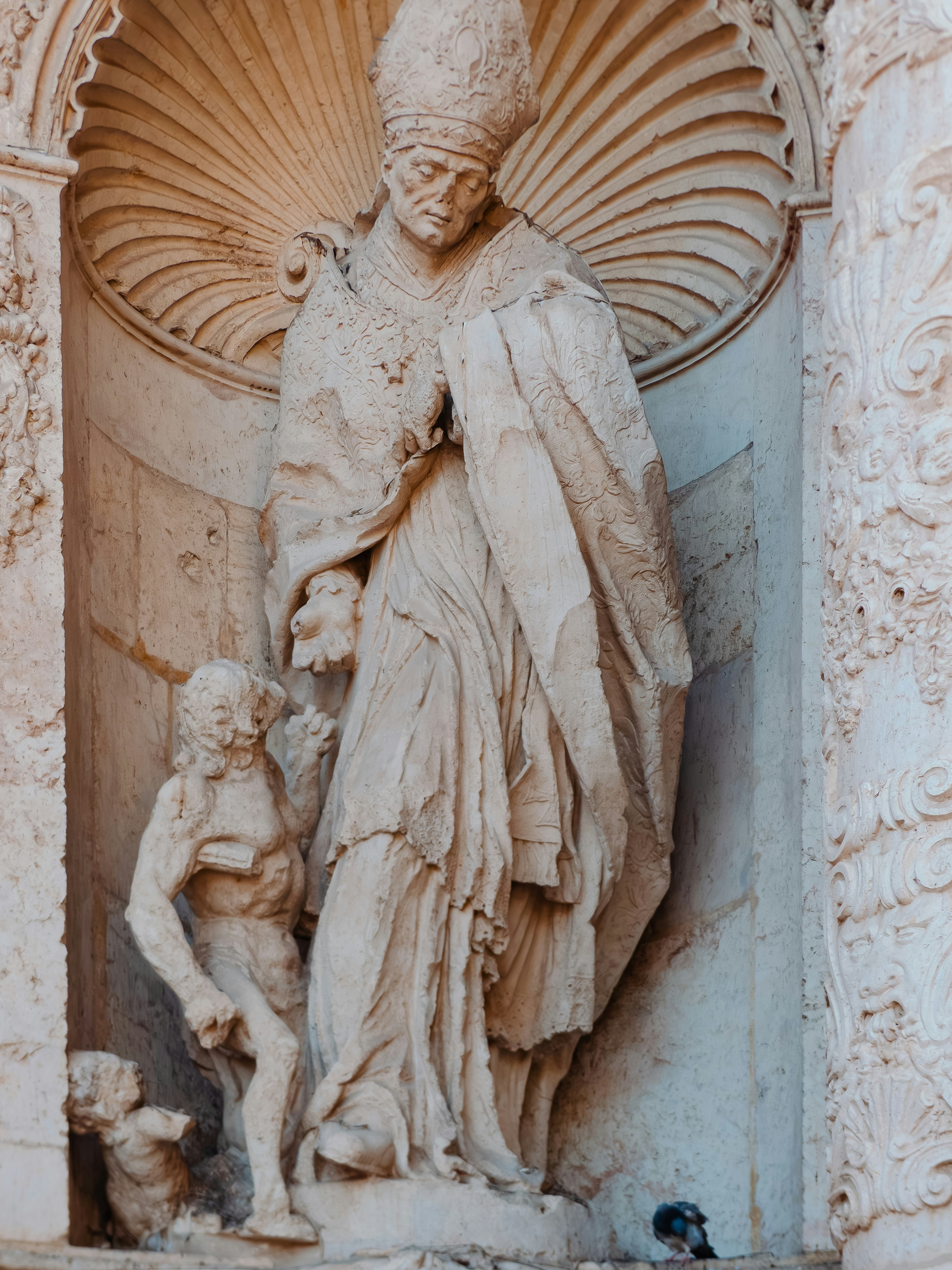 A stone statue of a pope in a niche with a smaller figure
