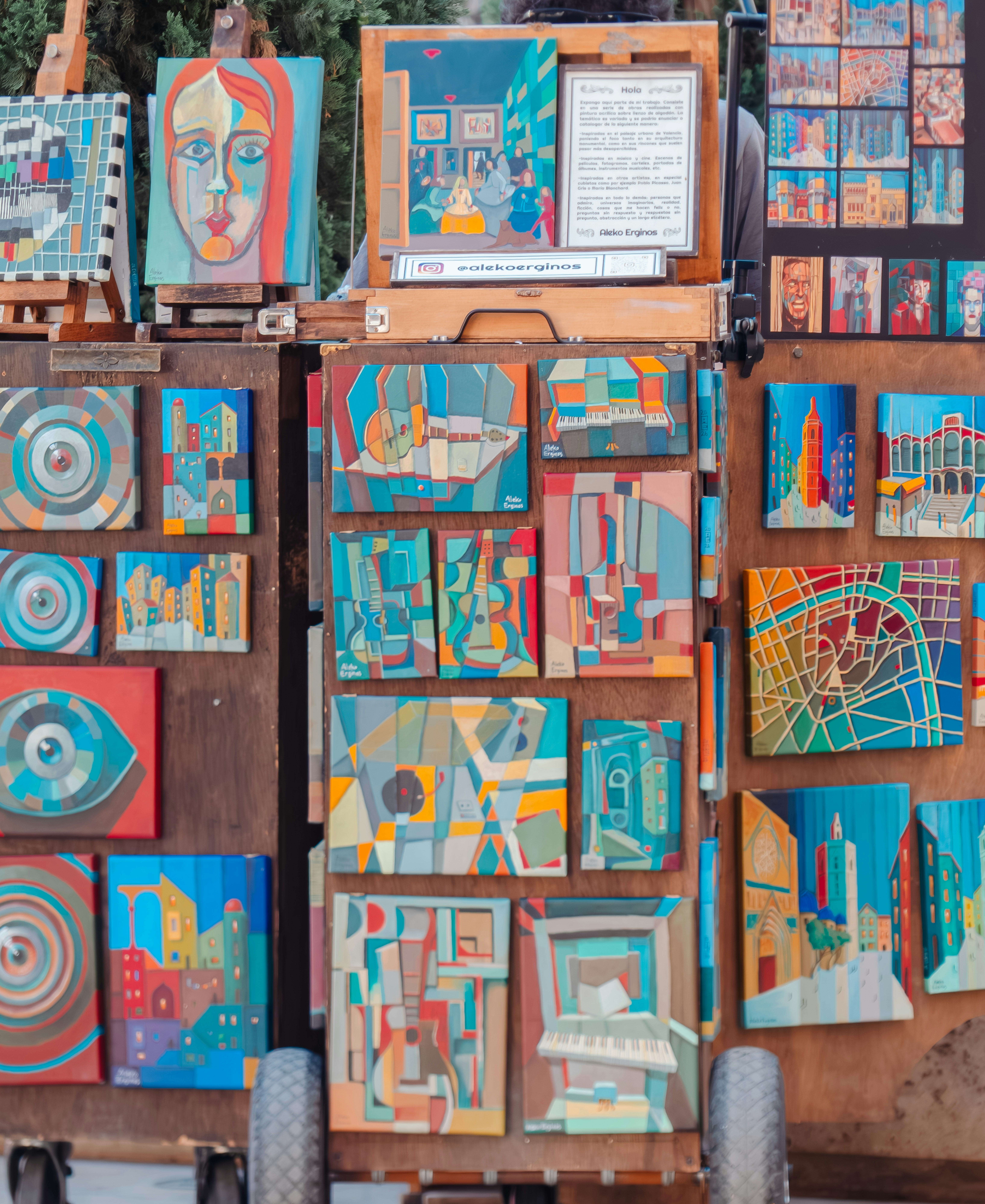 A wooden display cart covered in colorful cubist paintings of cityscapes and musical instruments