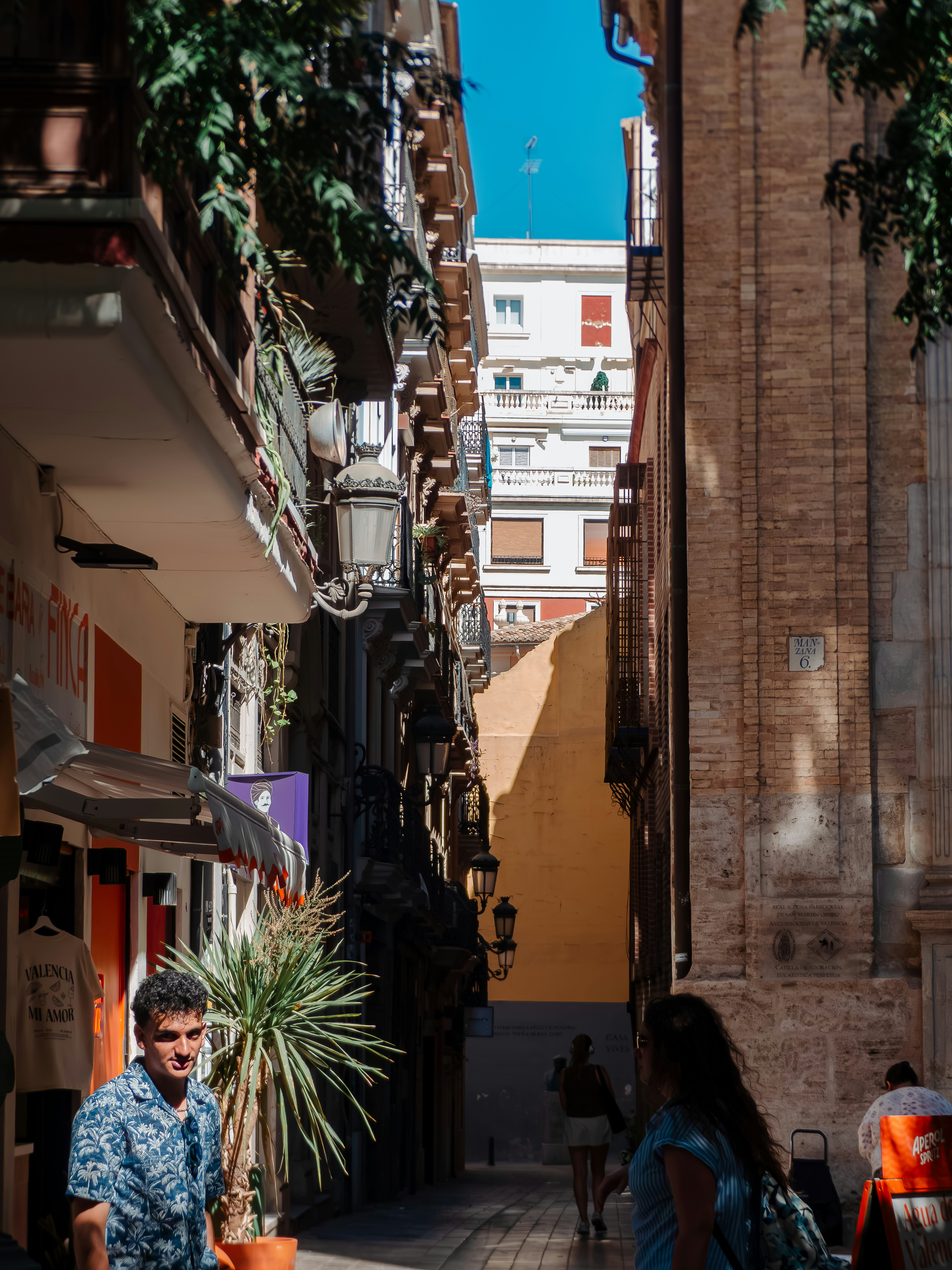 People walking through a narrow sunlit street lined with historic buildings in Valencia