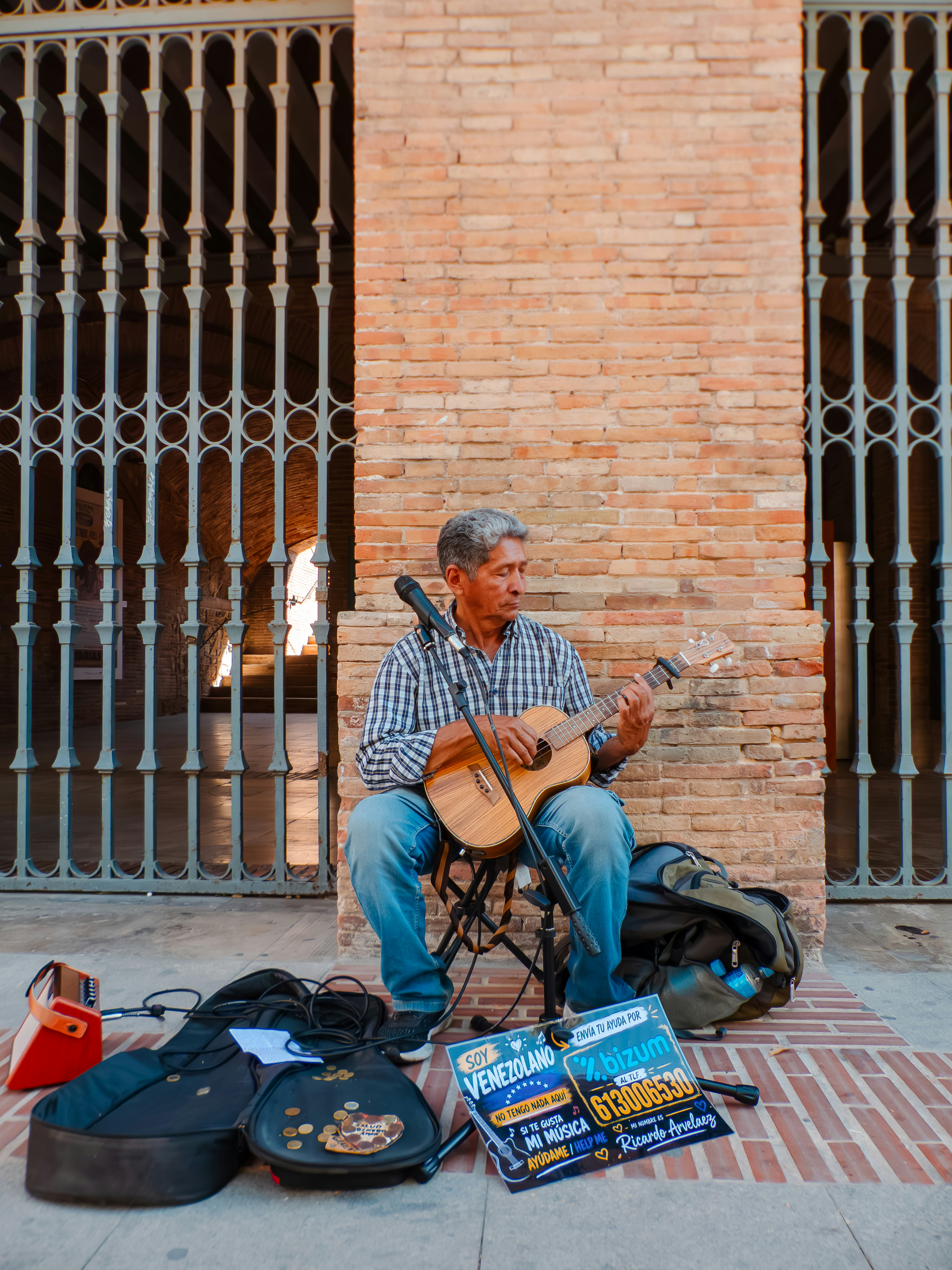A man playing a small acoustic guitar in front of a brick wall