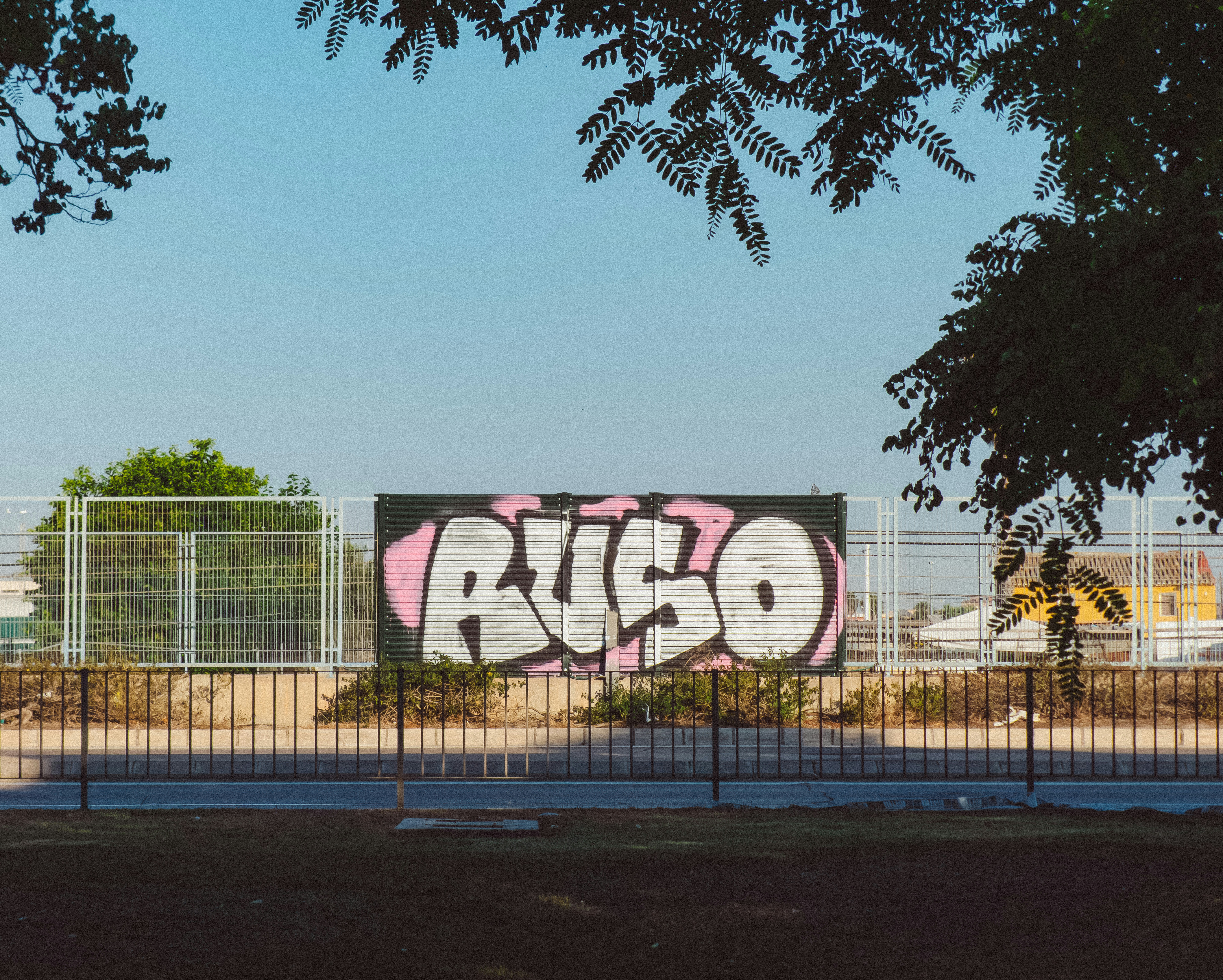 Graffiti reading "RUSO" in white and pink on a metal fence panel