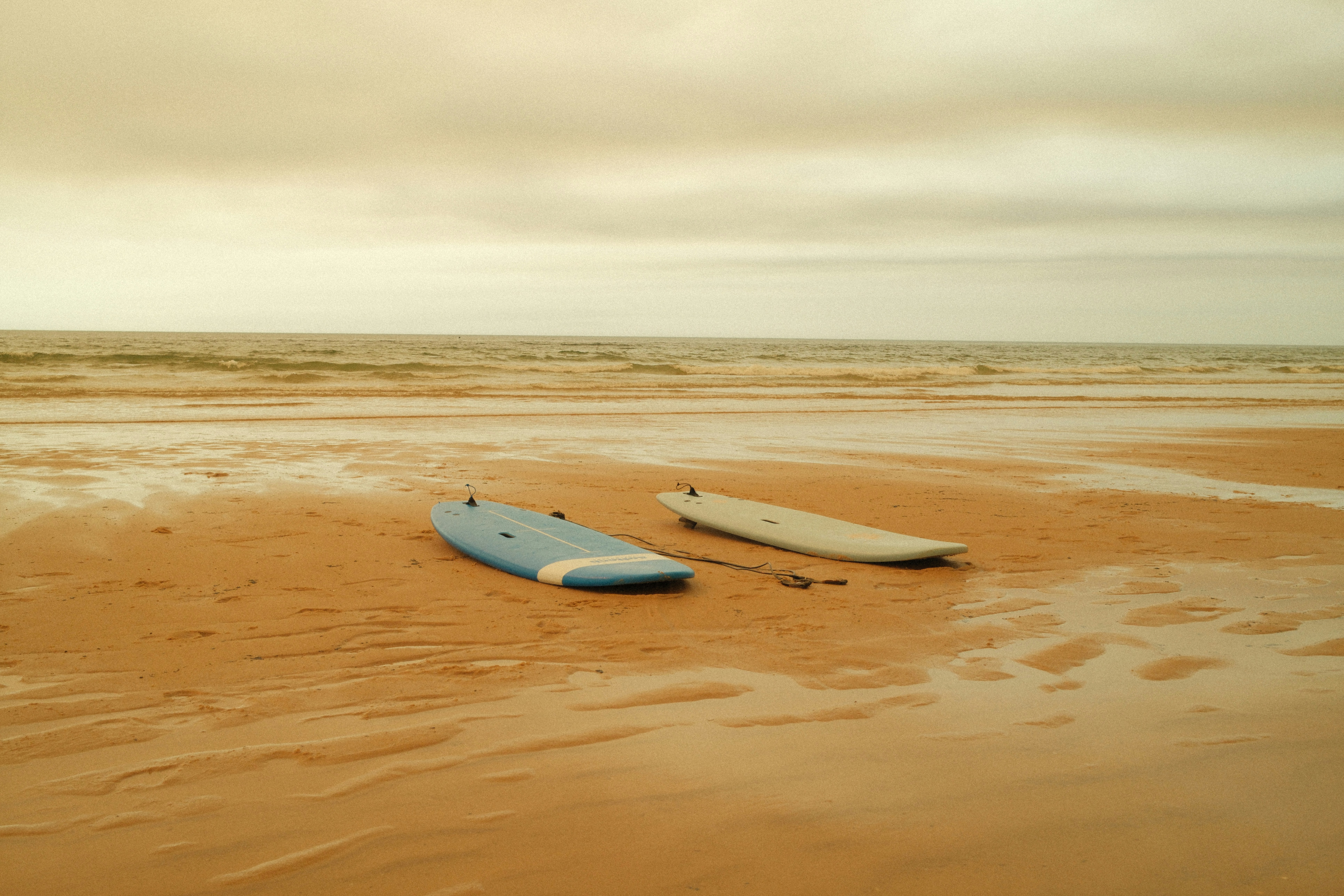 Deux planches de surf sur une plage de sable mouillée sous un ciel nuageux