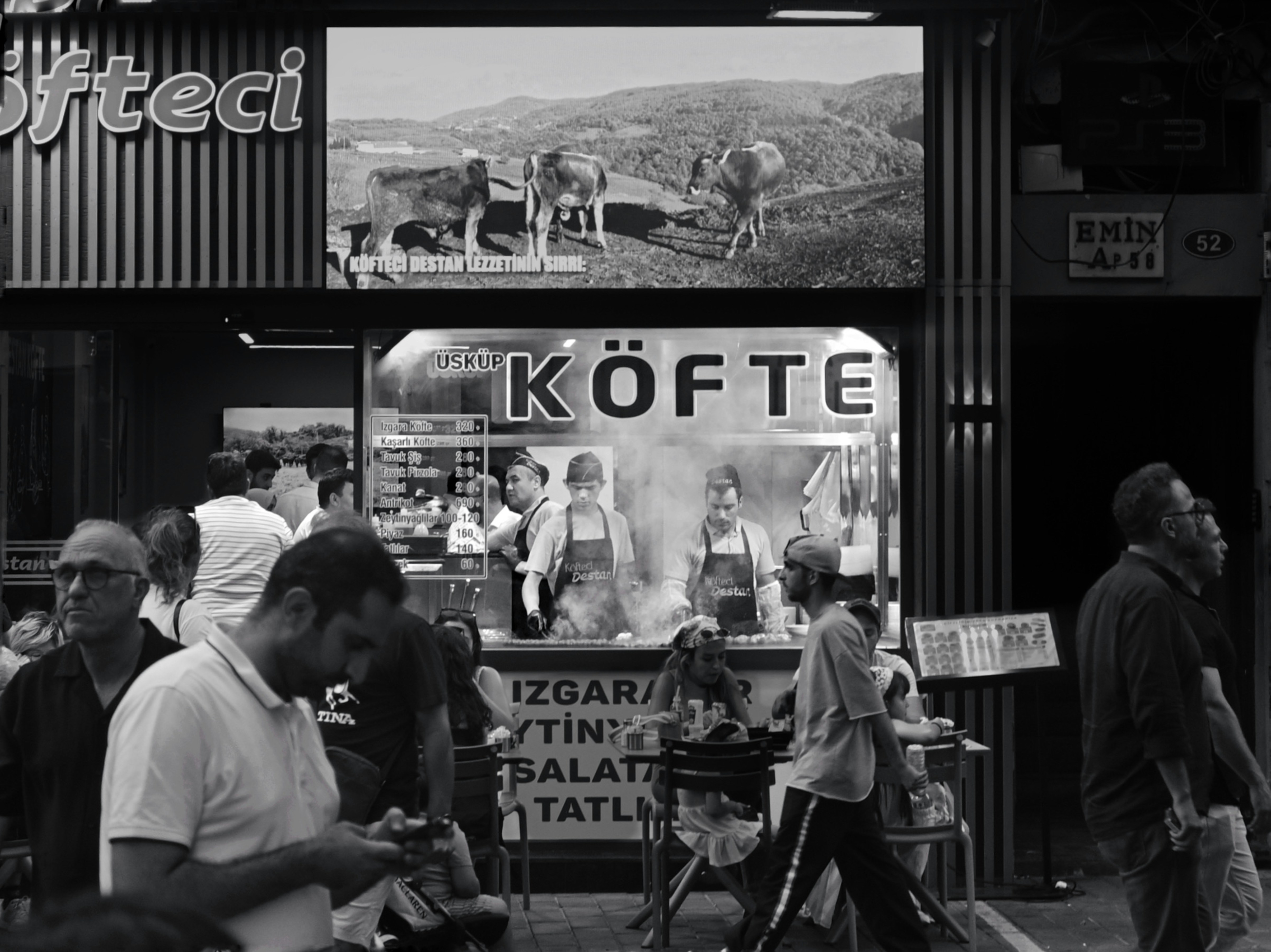 People walking past a restaurant with cooks grilling meat in a smoky kitchen