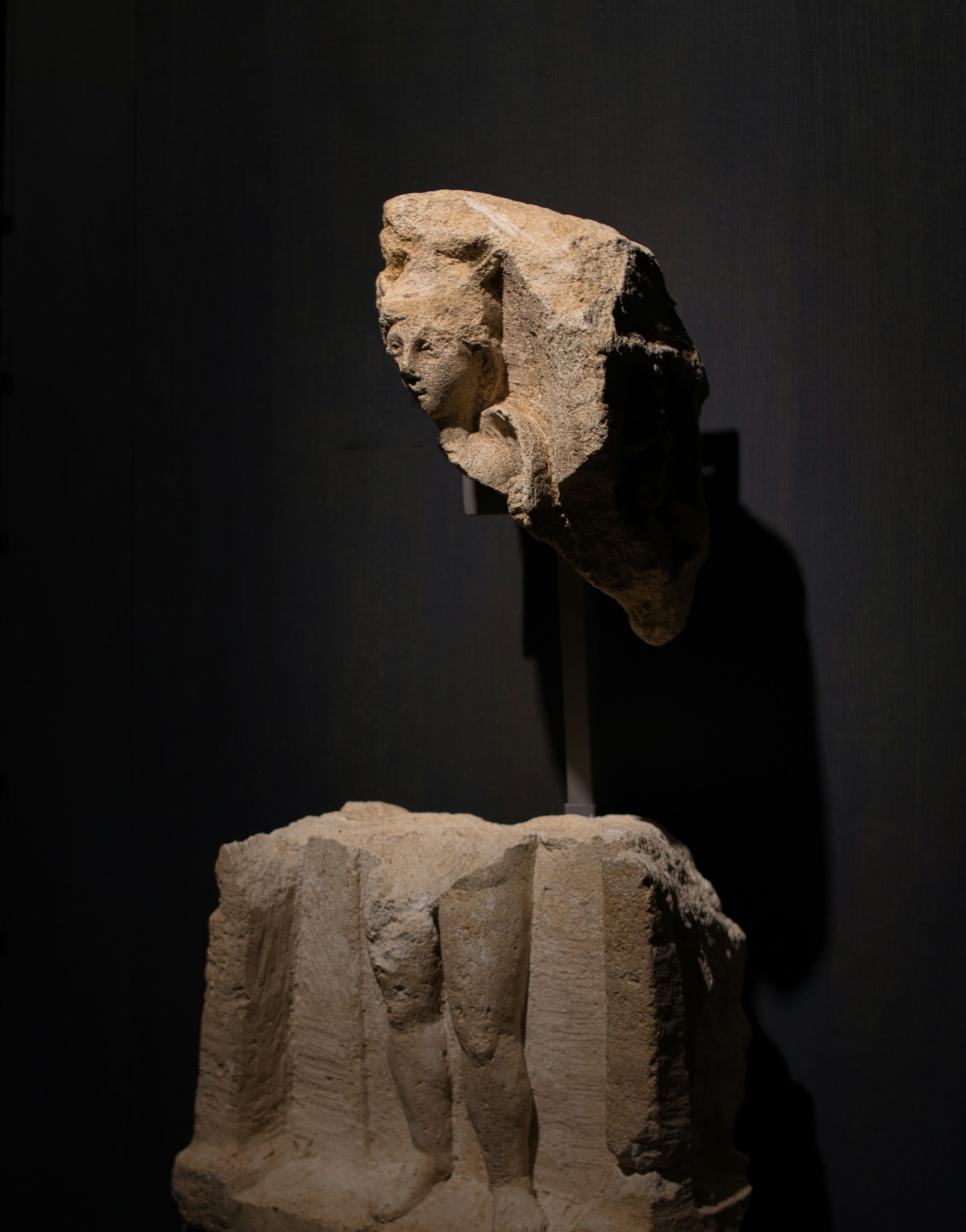 Una escultura fragmentada de piedra de una figura humana sobre un fondo oscuro.