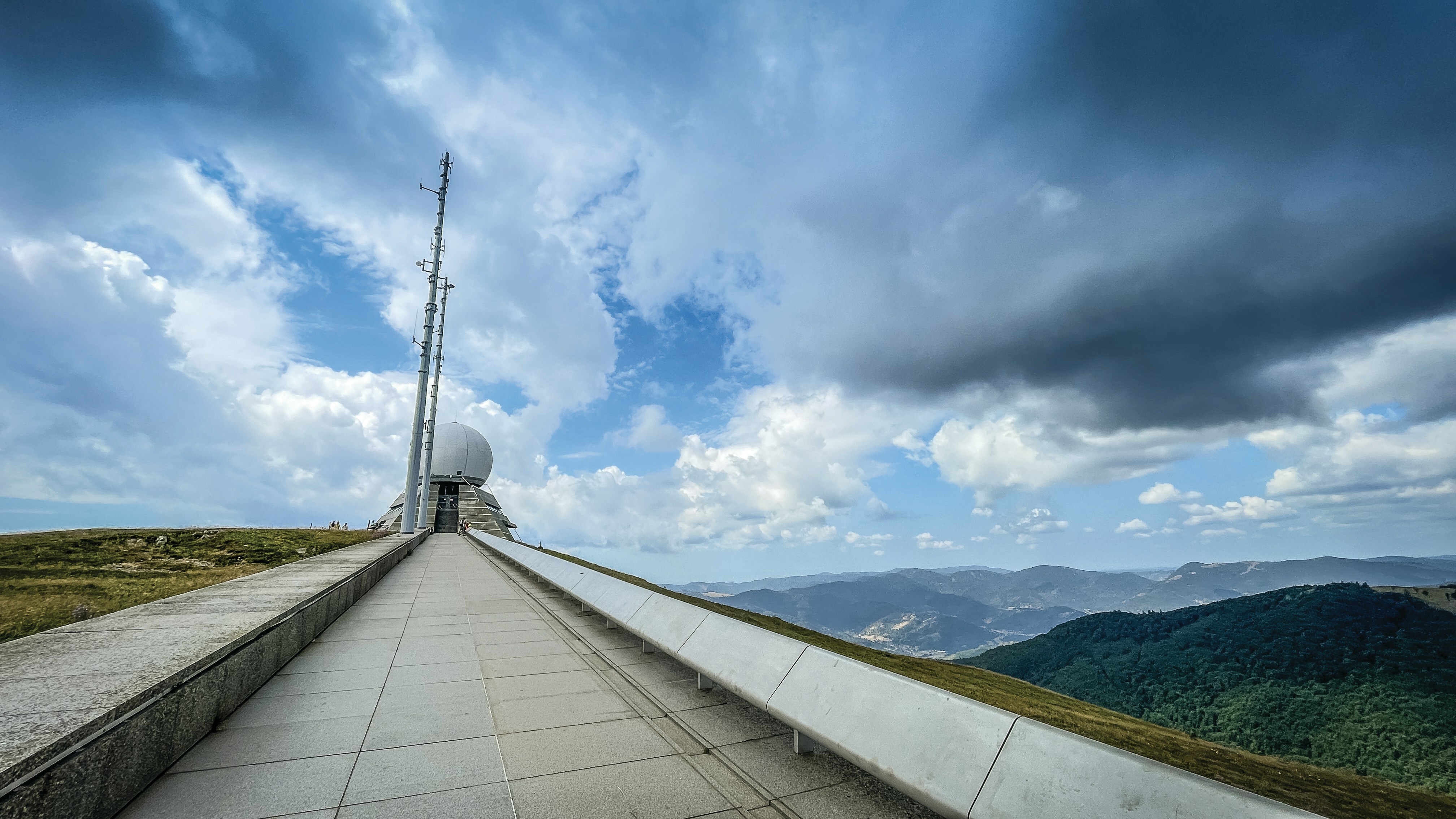Modern radar station on a mountaintop under a dramatic sky.