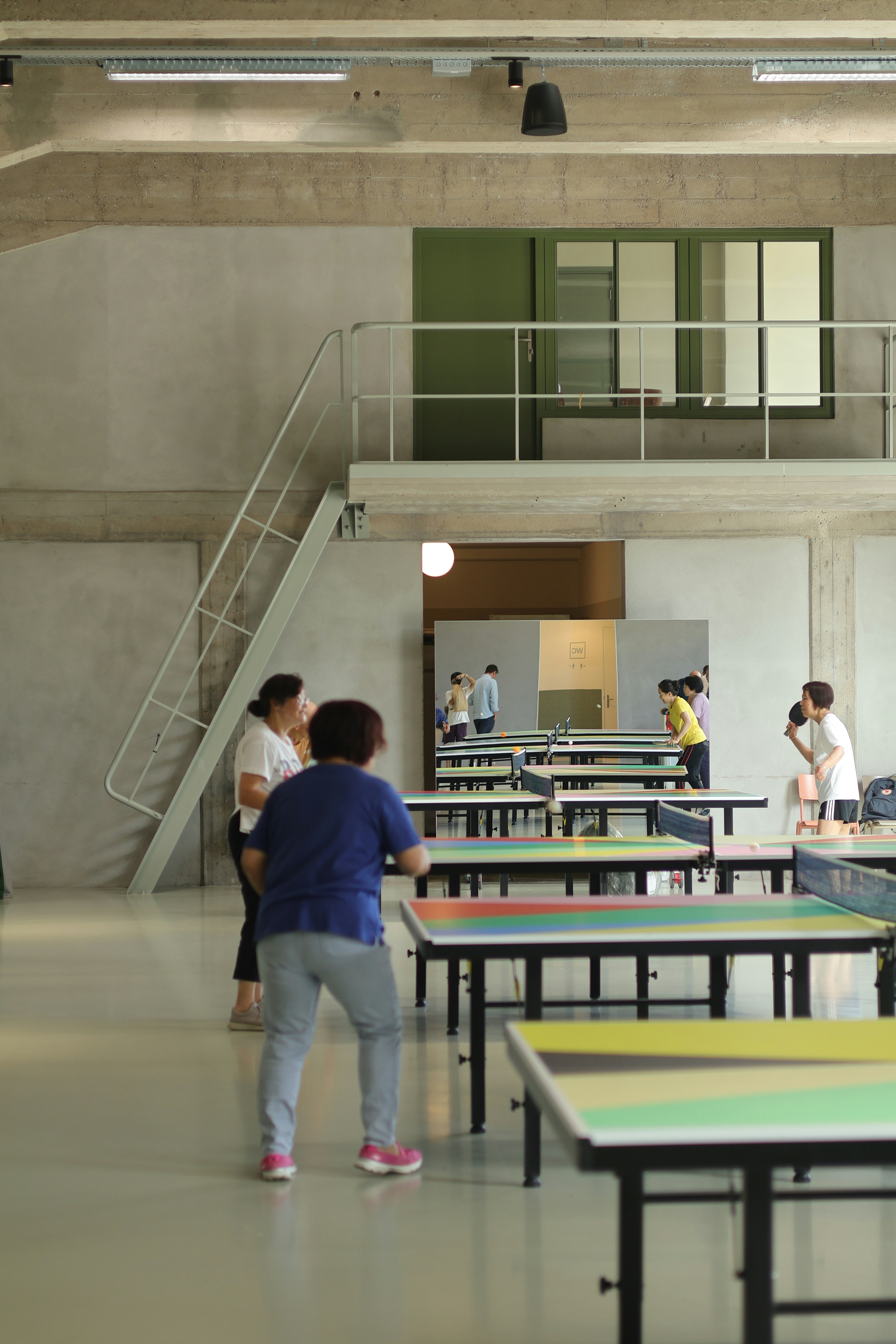 People playing table tennis on colorful tables in a large industrial style room