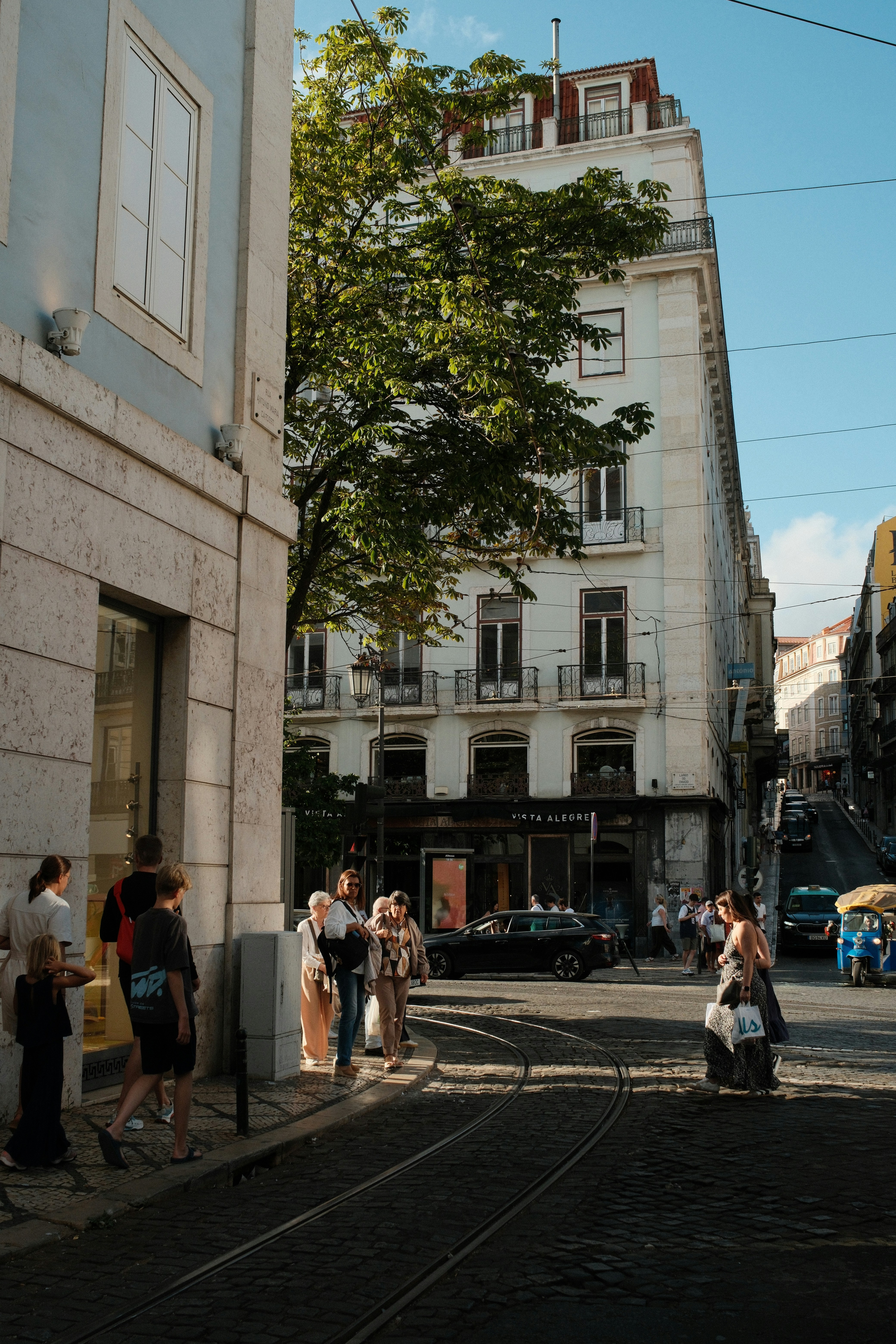 People walking on a cobblestone street with tram tracks in Lisbon, Portugal