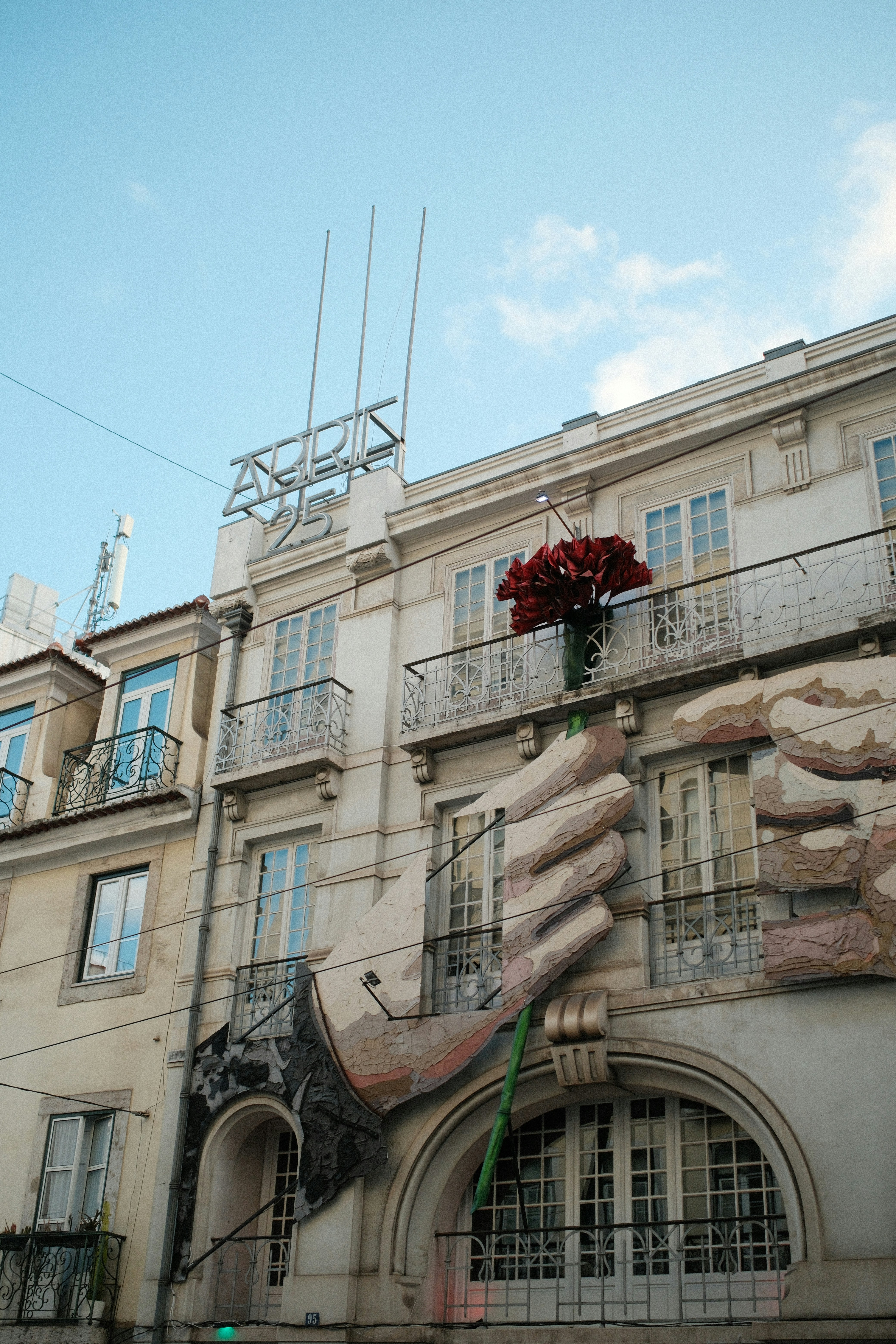A large sculpture of a hand holding a red flower on a building facade