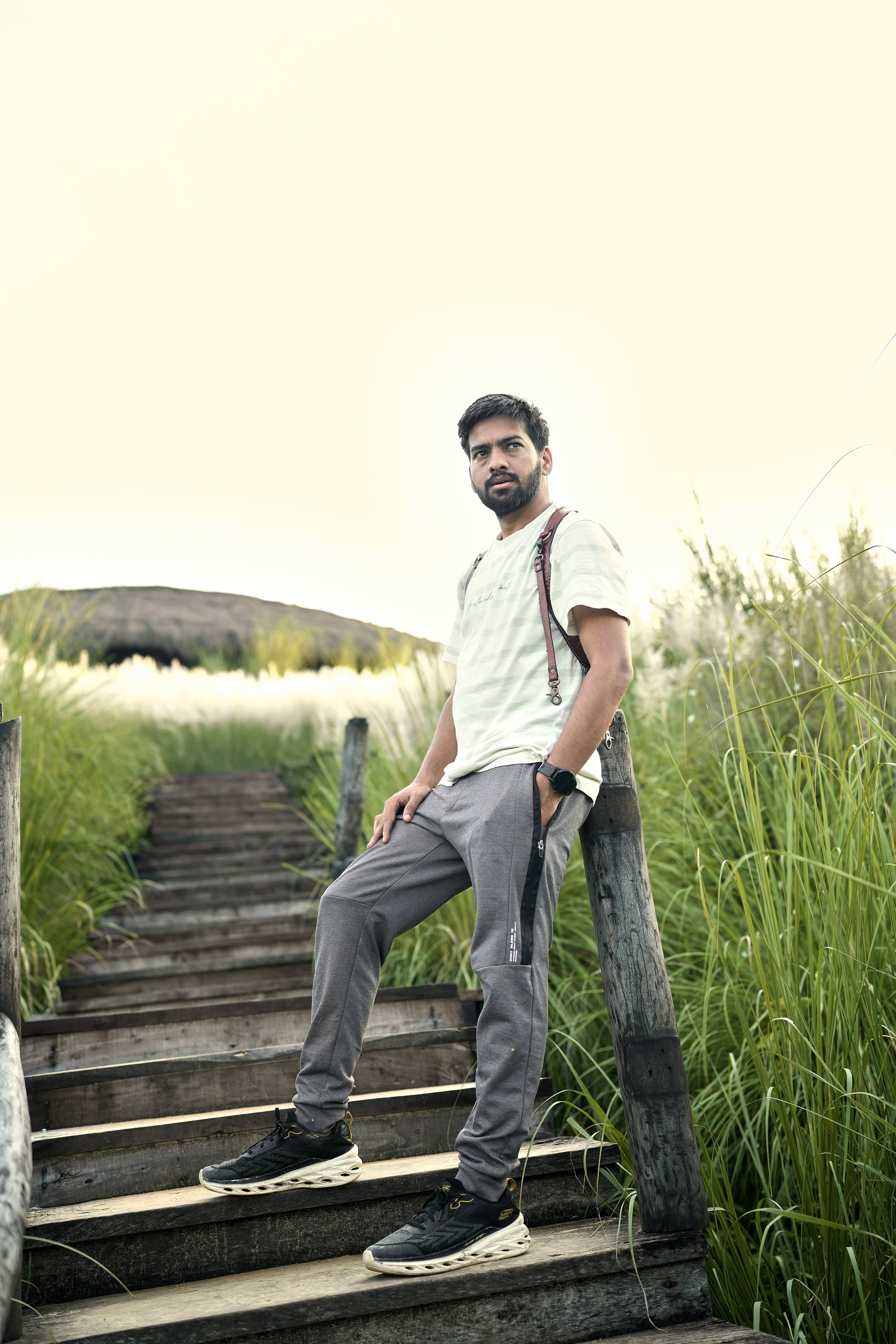 A man in a light t-shirt and grey joggers on a wooden staircase.