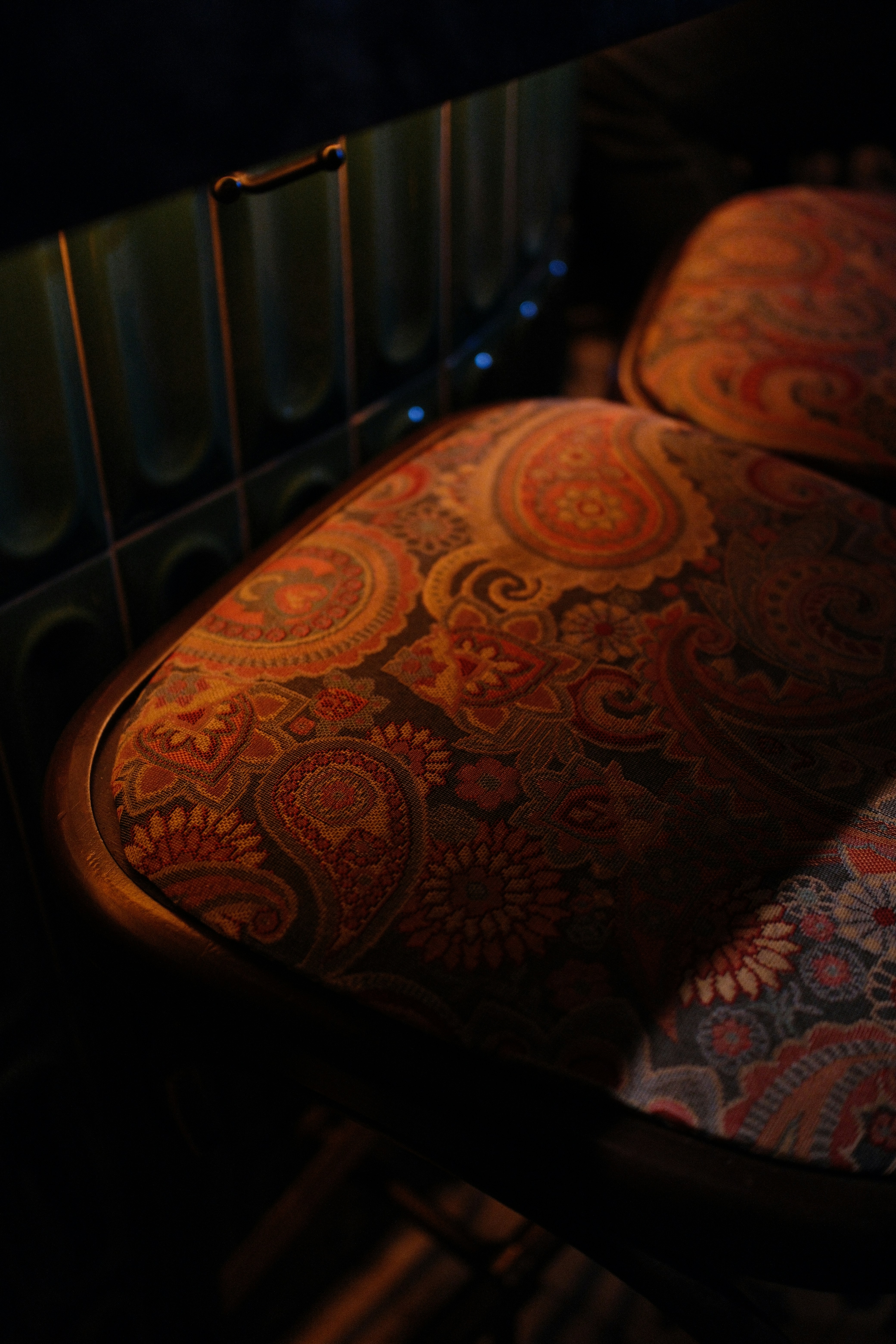 Two bar stools with patterned paisley fabric cushions beside a dark green tiled counter