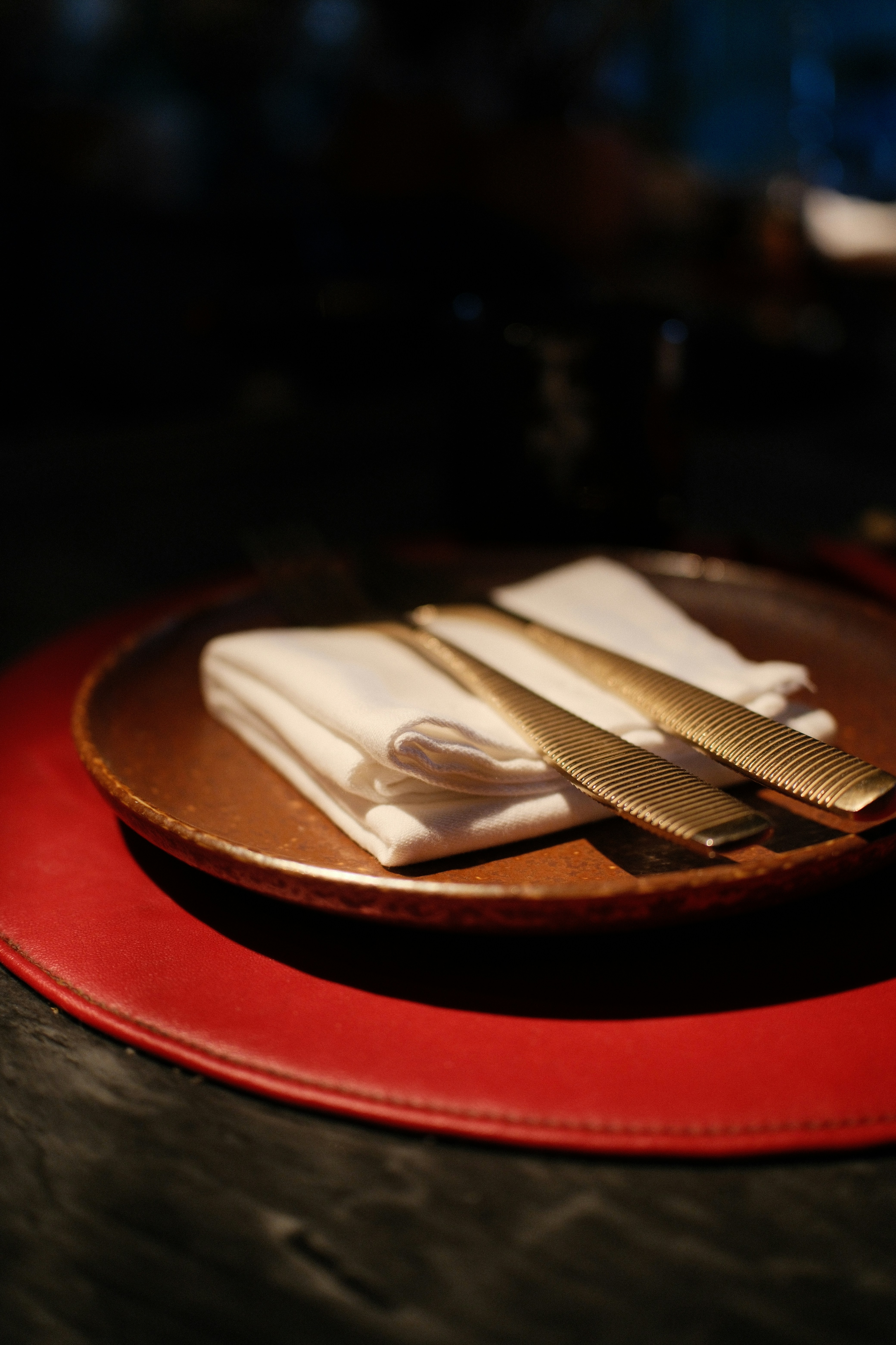 A white napkin and gold cutlery on a brown plate atop a red placemat