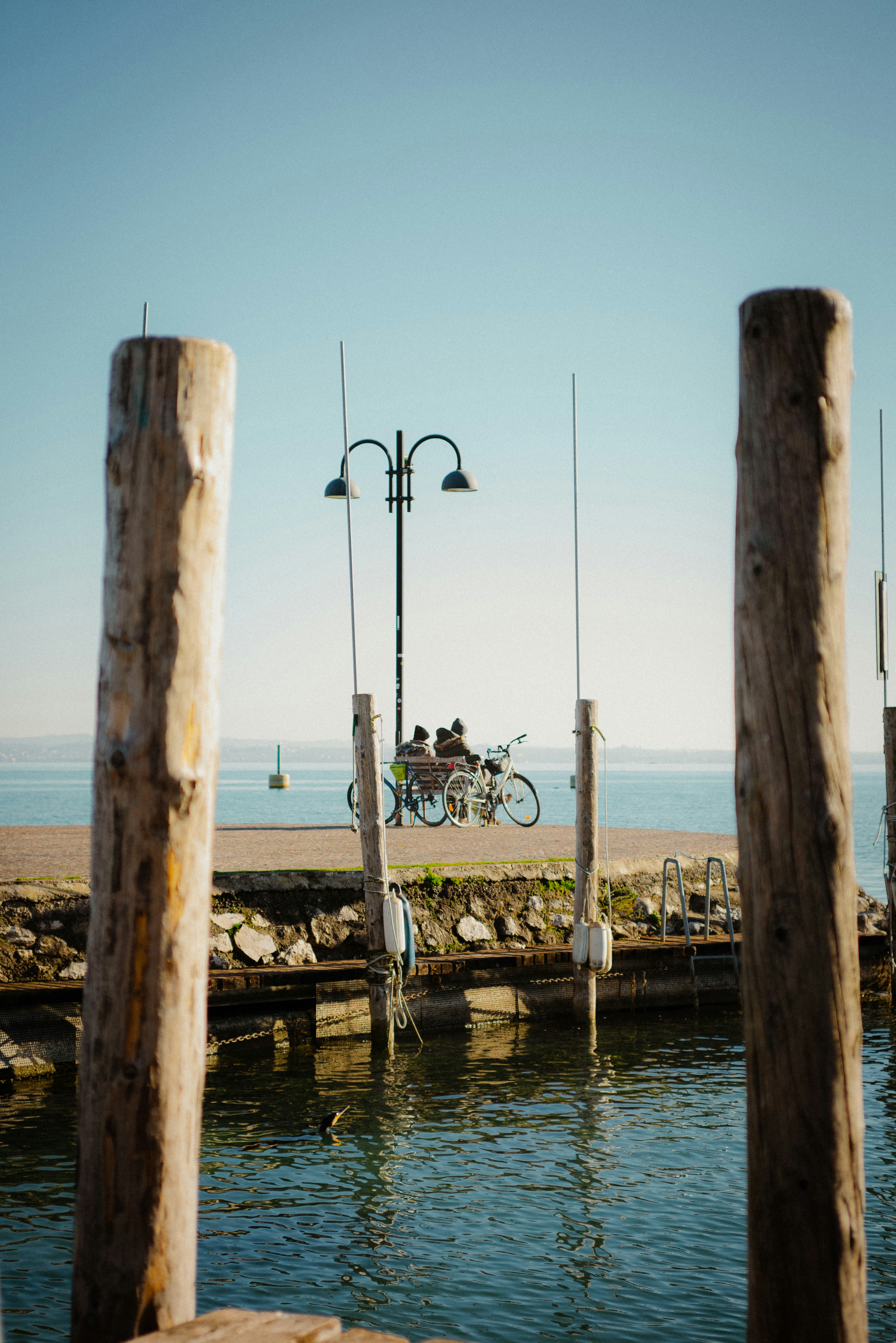 Two people on bicycles on a stone pier by a calm lake