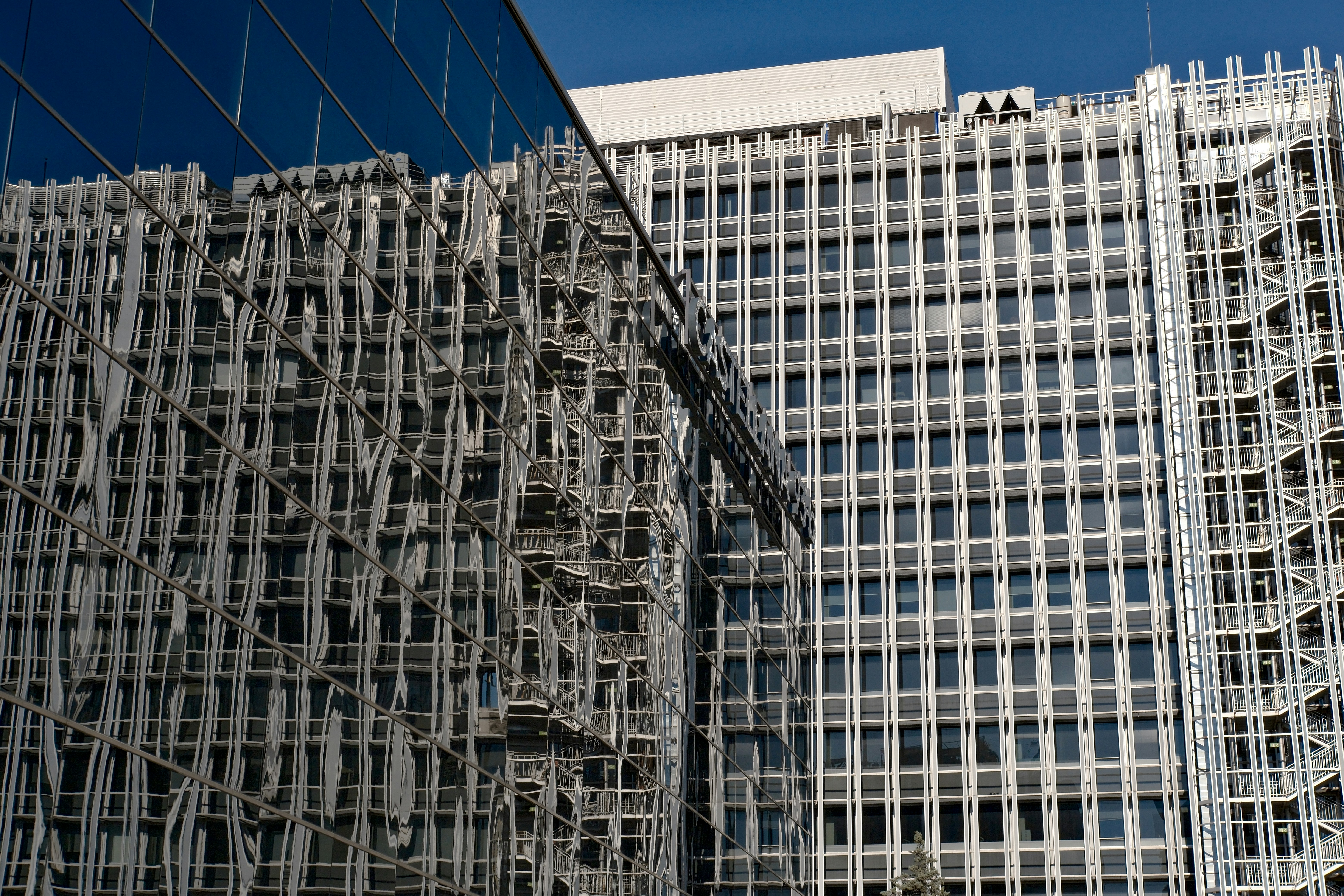 The lines of one skyscraper are distorted in the glass reflection from another.