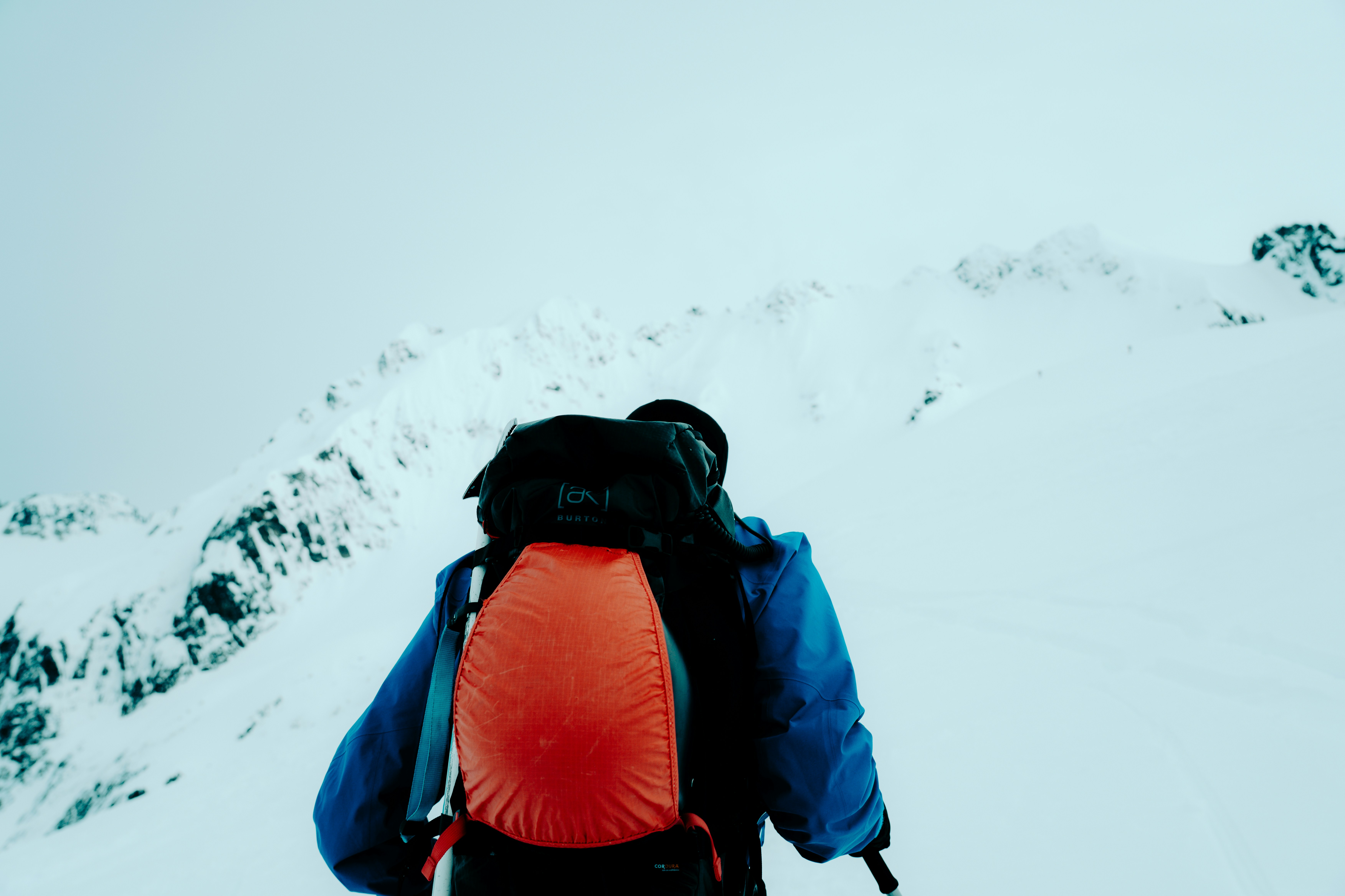Hiker with orange backpack ascends a snow-covered mountain.