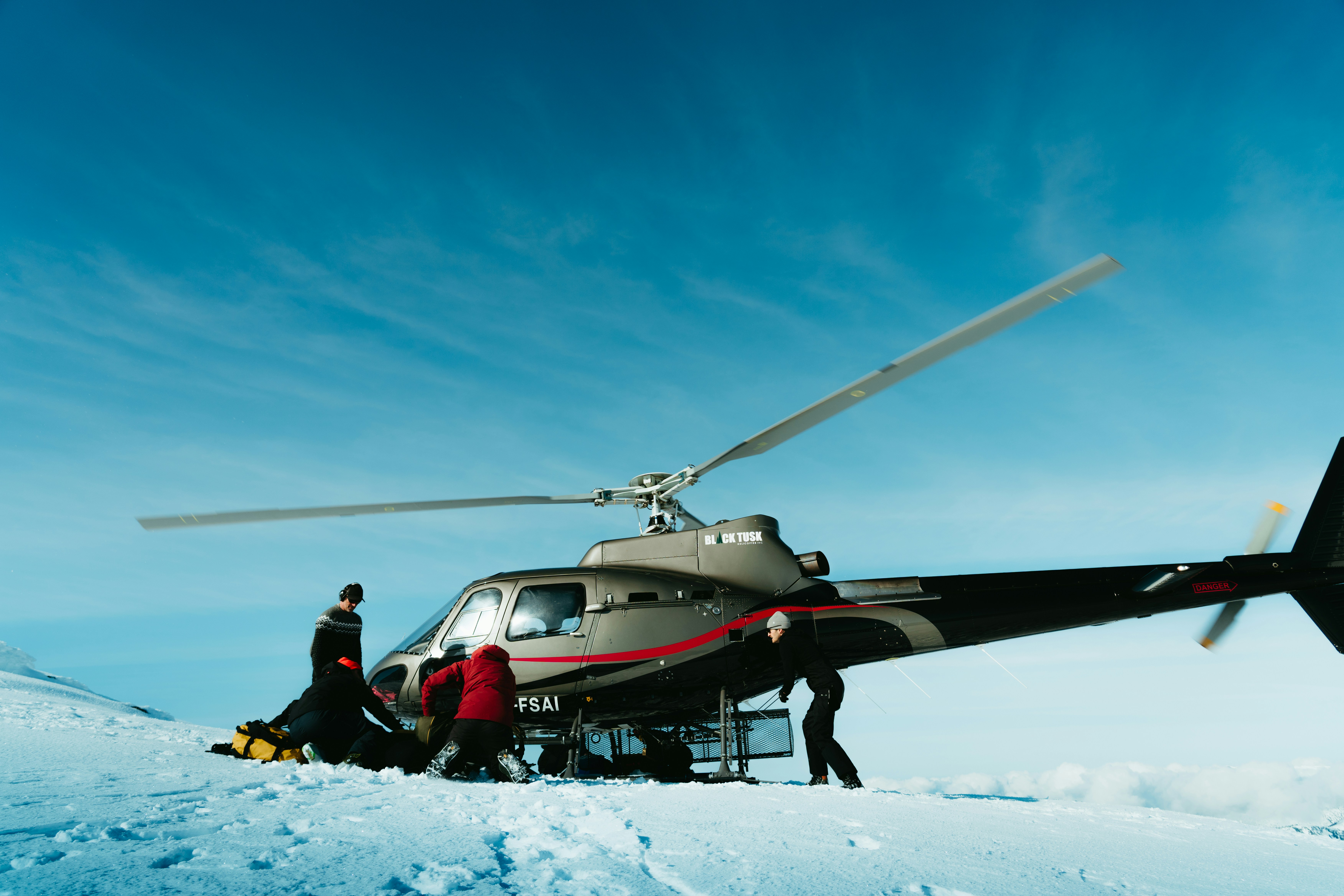 A helicopter landed on a snowy mountain with people nearby.