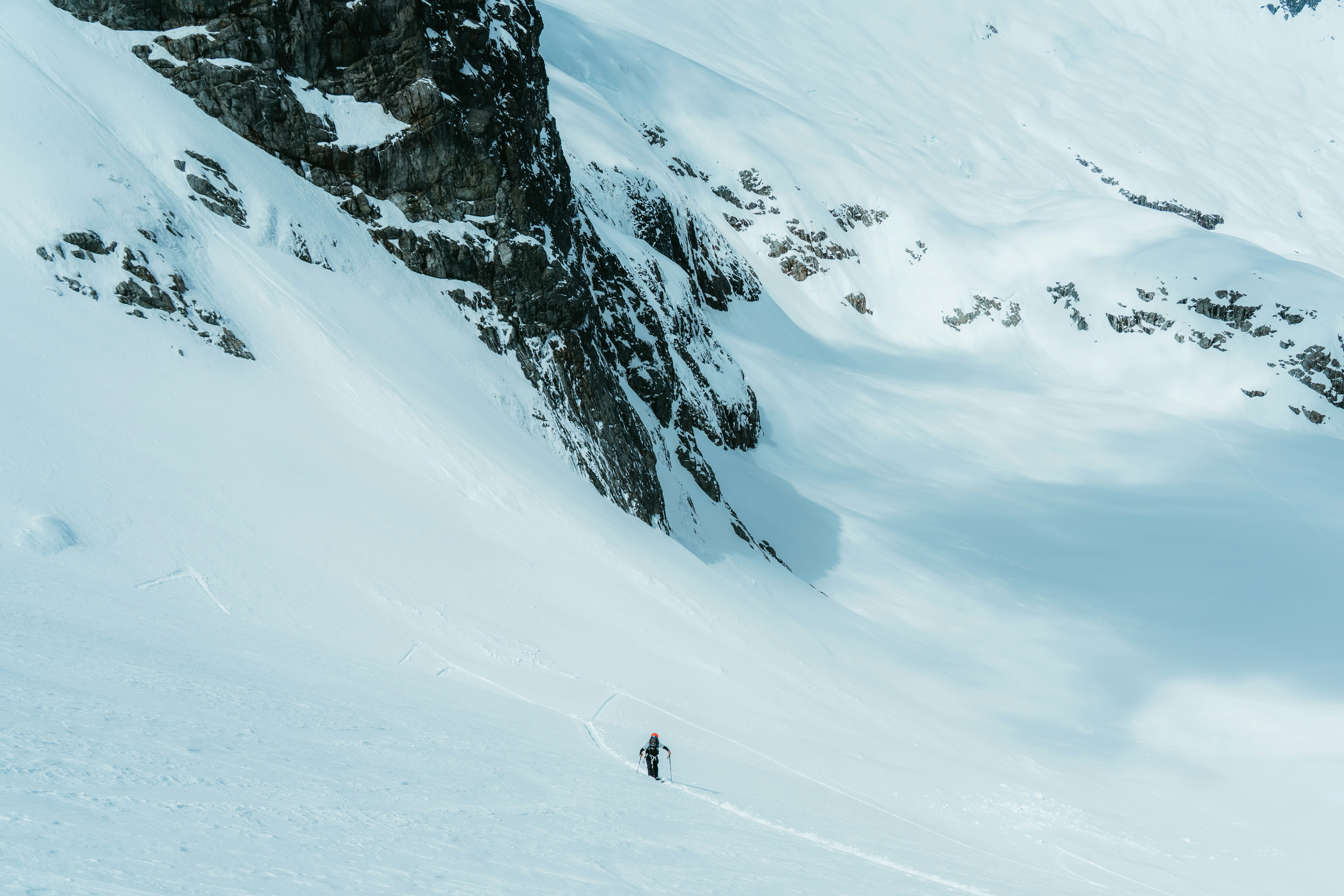 A lone skier descends a vast, snowy mountain slope.