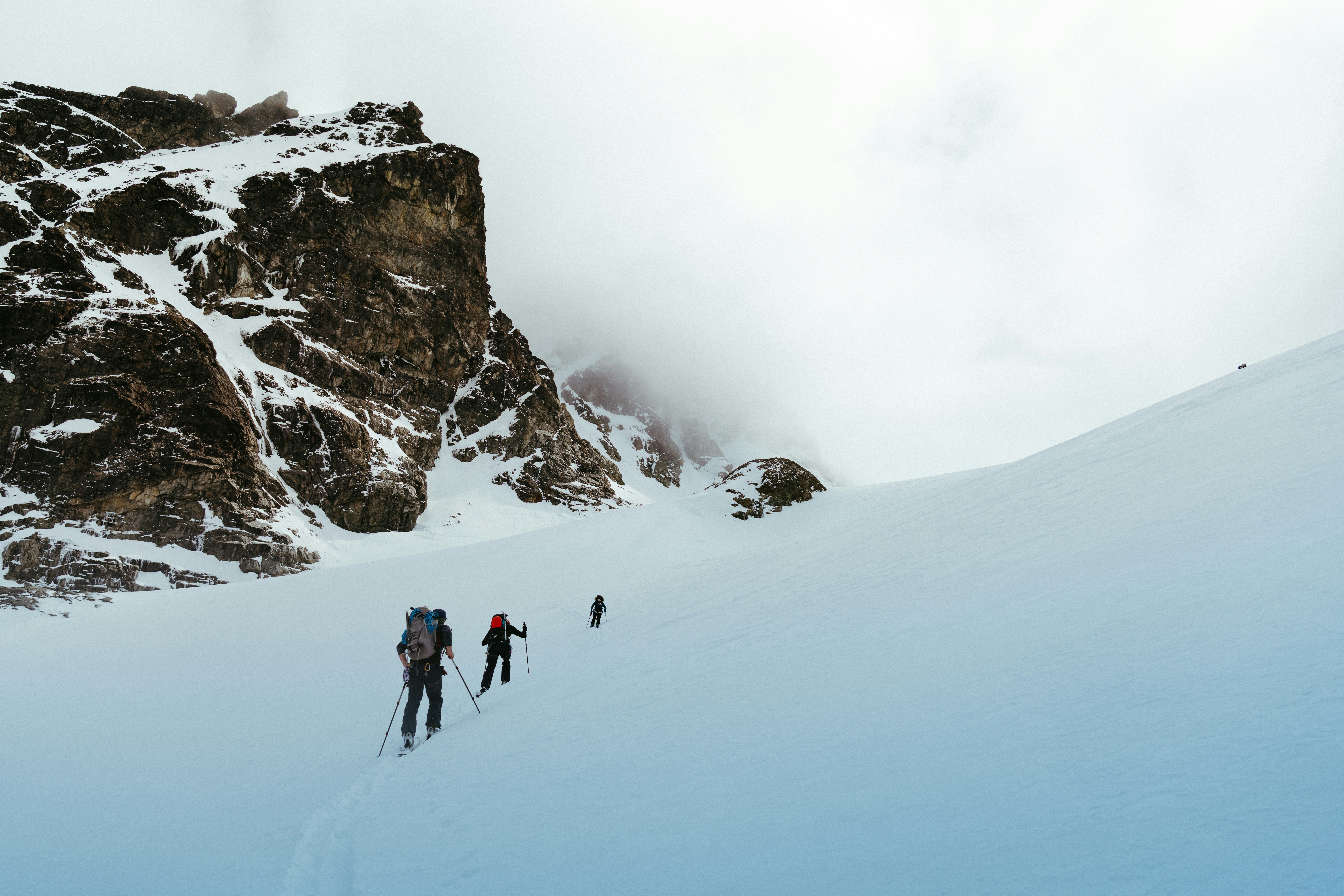 People skiing up a snowy mountain with a rocky cliff.