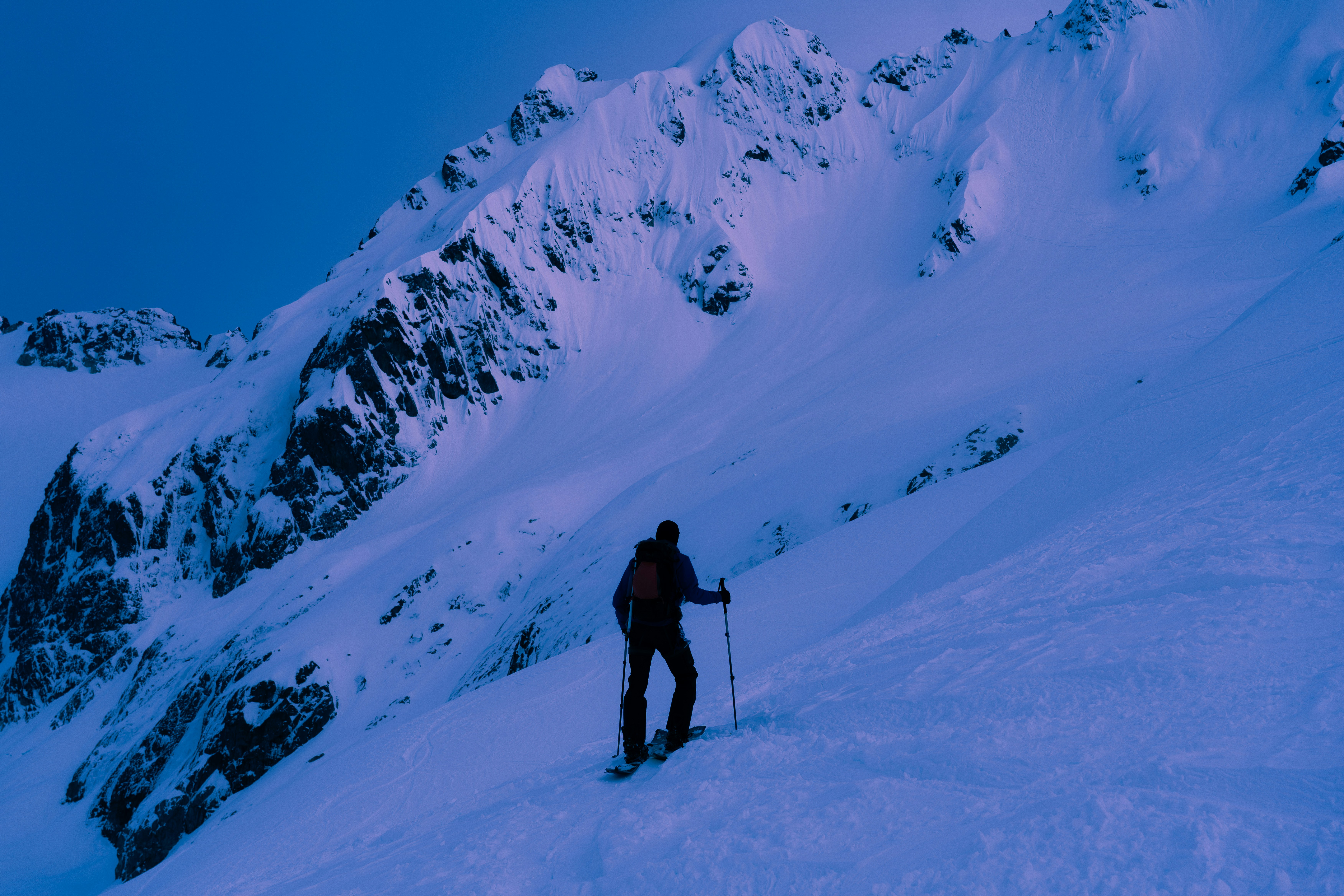 Backcountry skier ascends a snowy mountain peak.