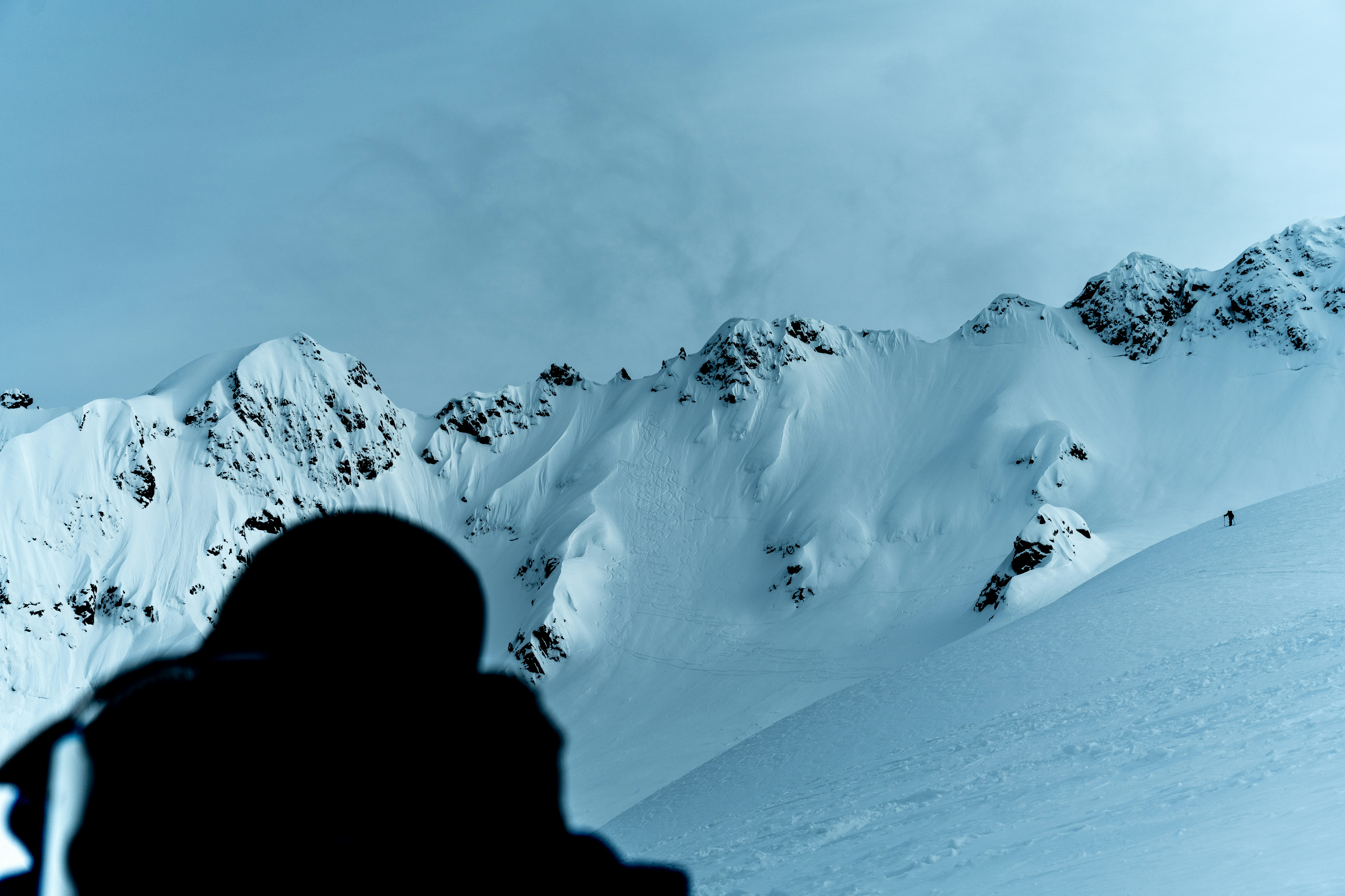 Dark silhouette observes expansive snow-capped mountains.