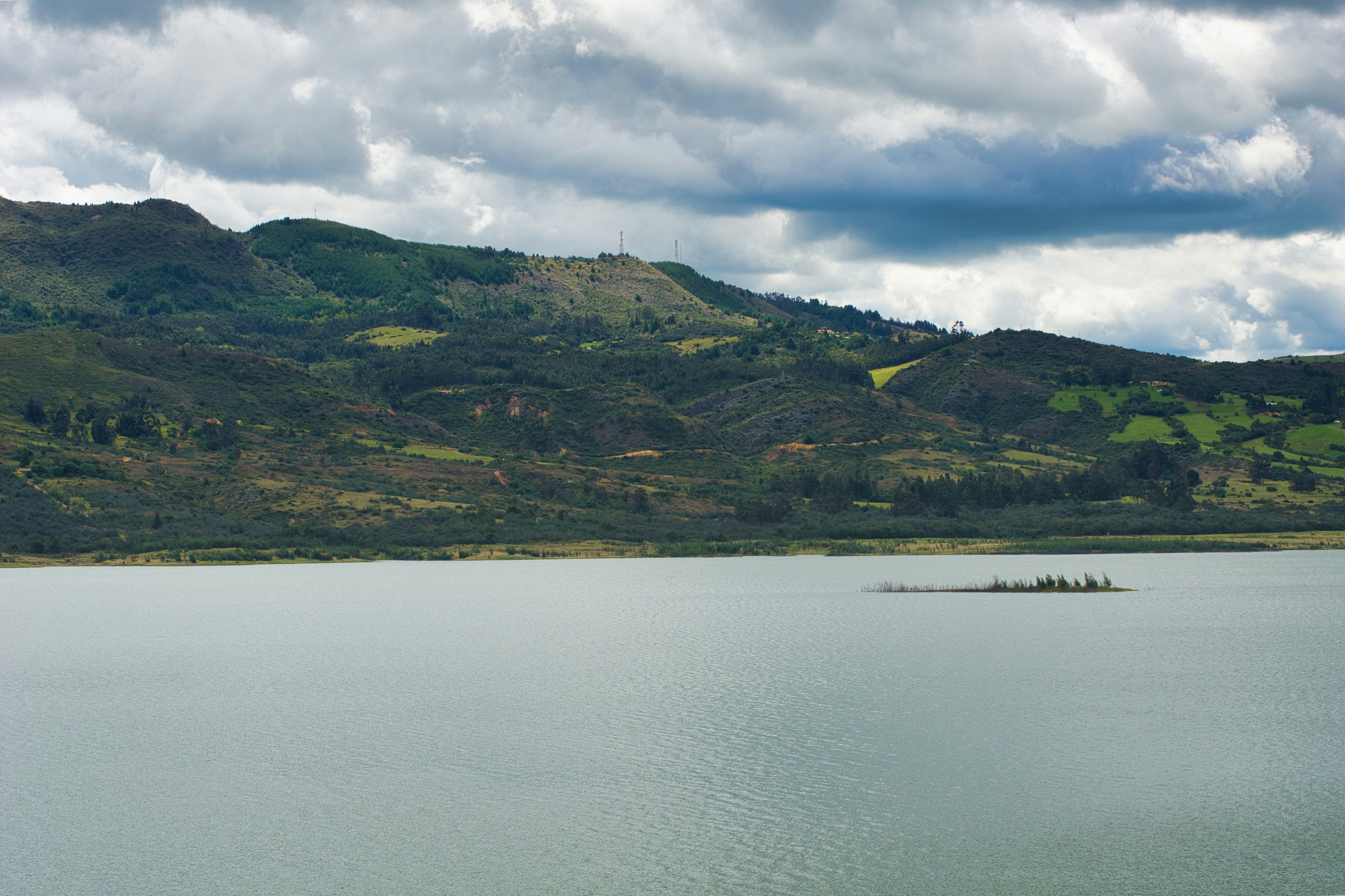 A serene lake with green mountains under a cloudy sky