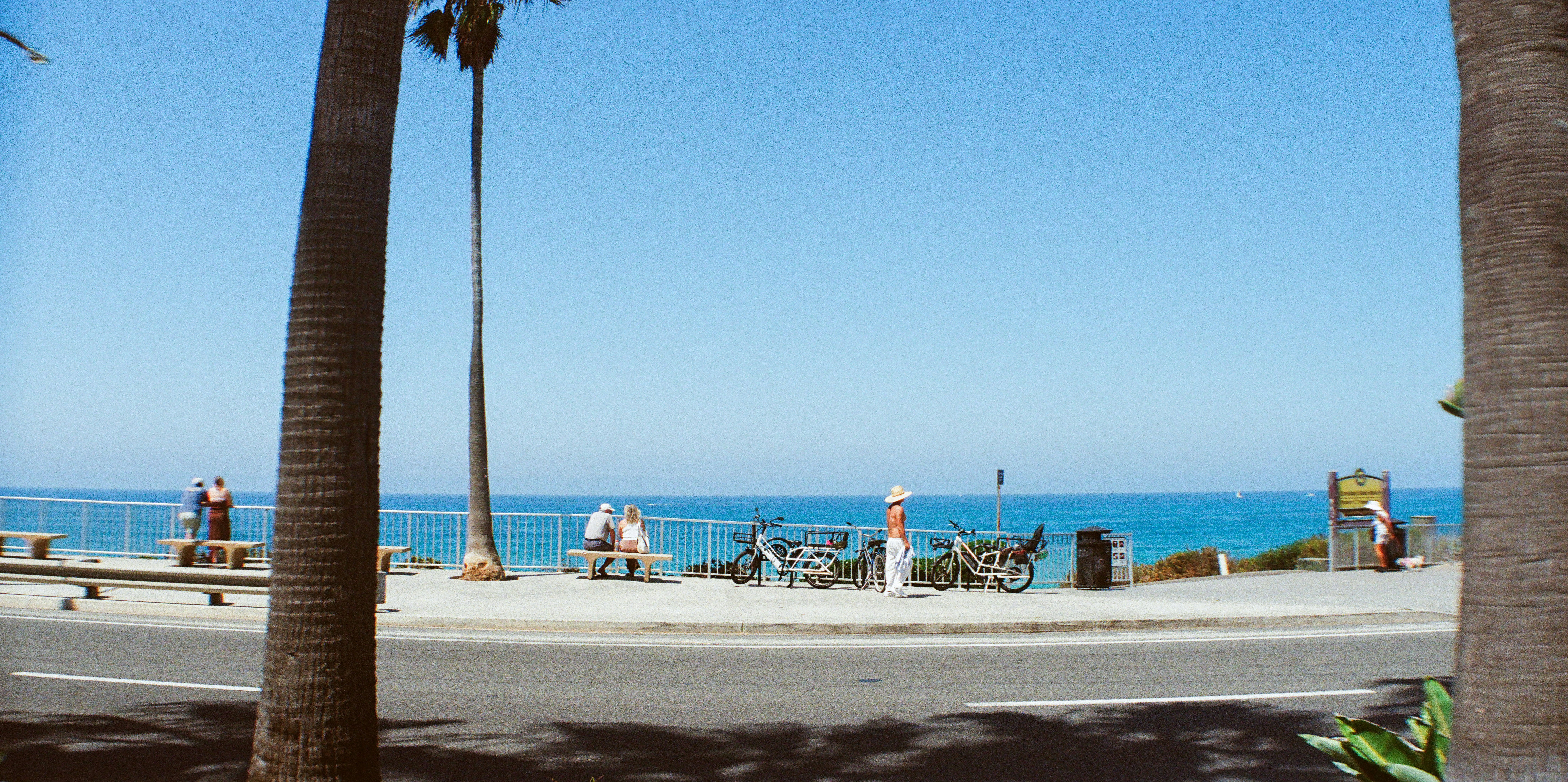Sunny coastal promenade with people, bicycles, and blue ocean