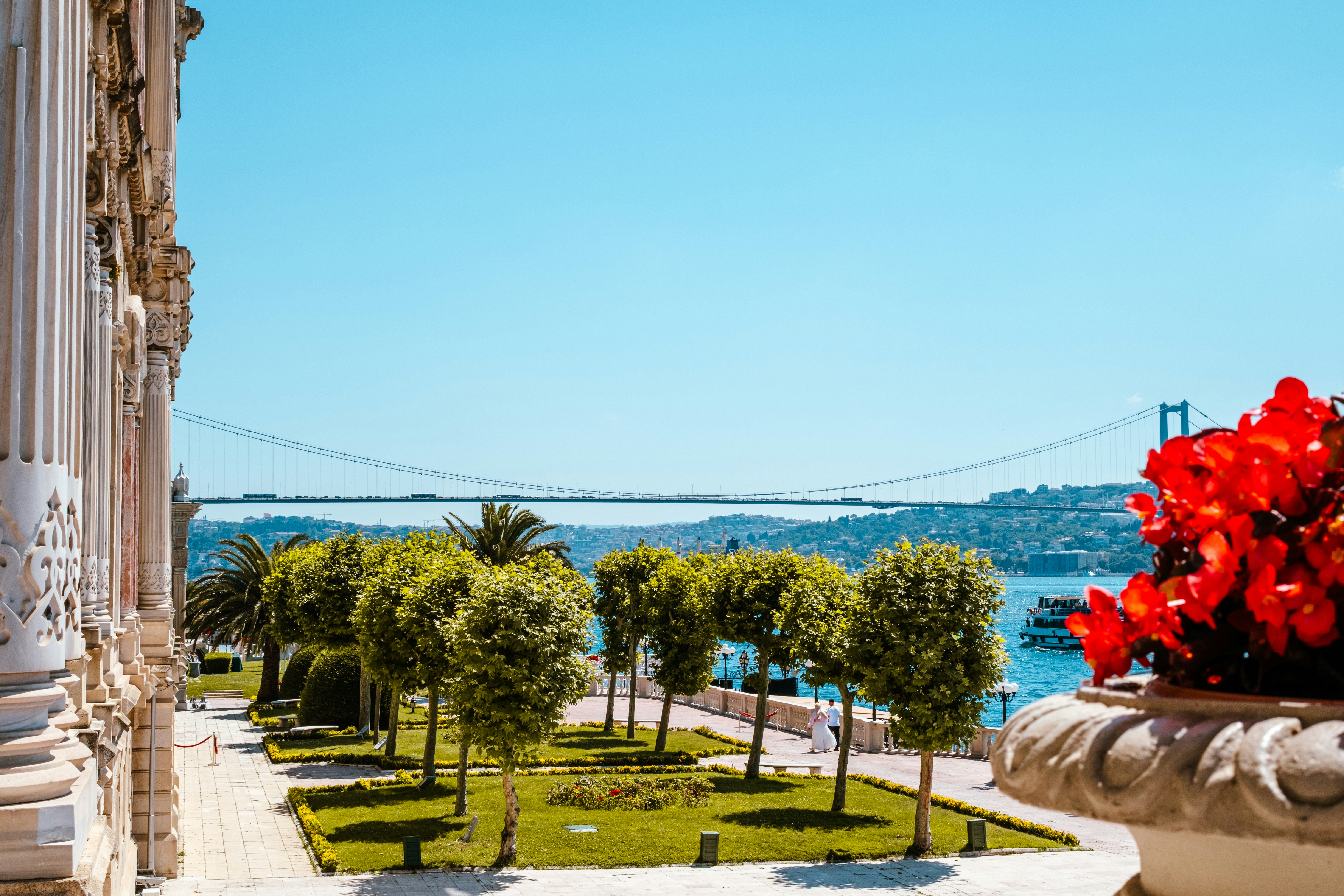Grand palace facade, garden, bosphorus, and bridge under blue sky