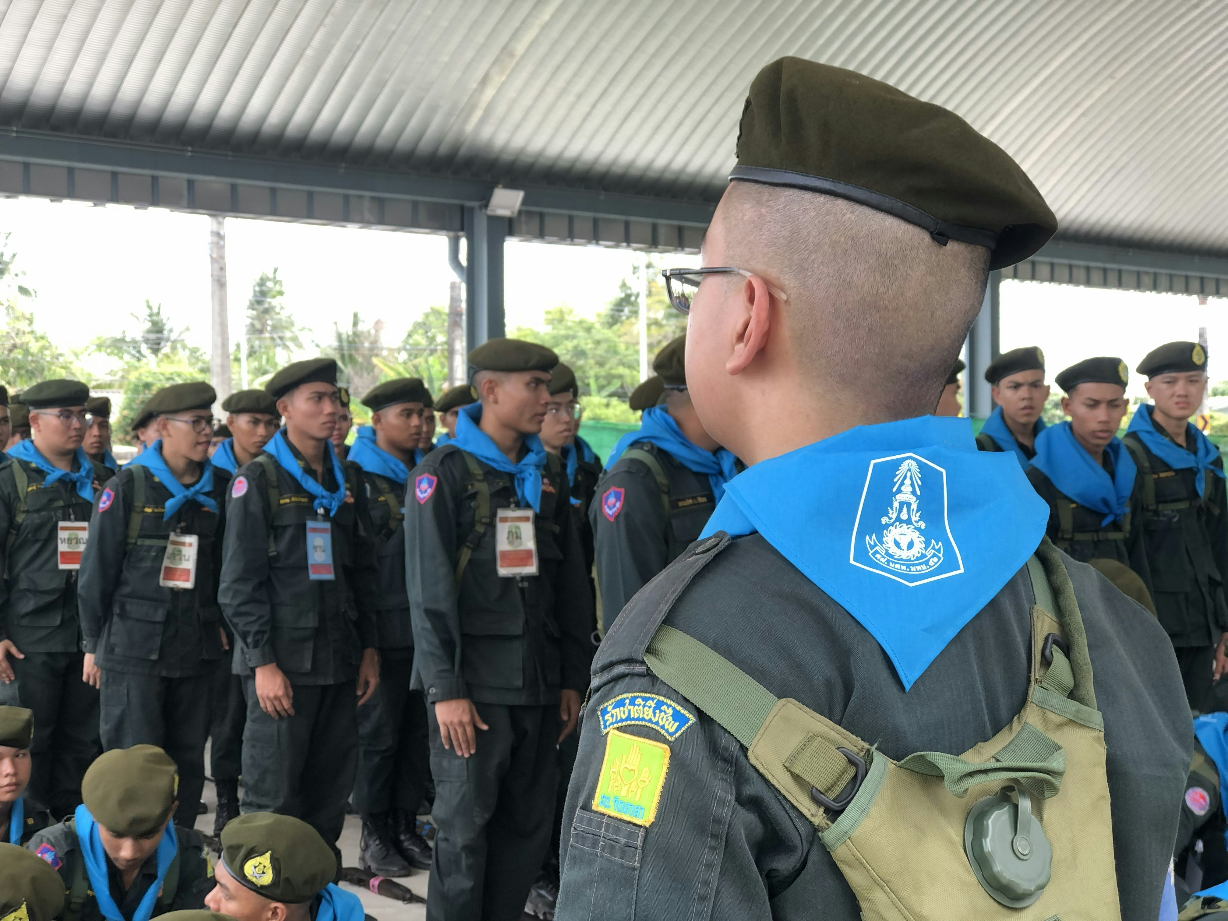 Young men in military uniforms and blue scarves stand outdoors
