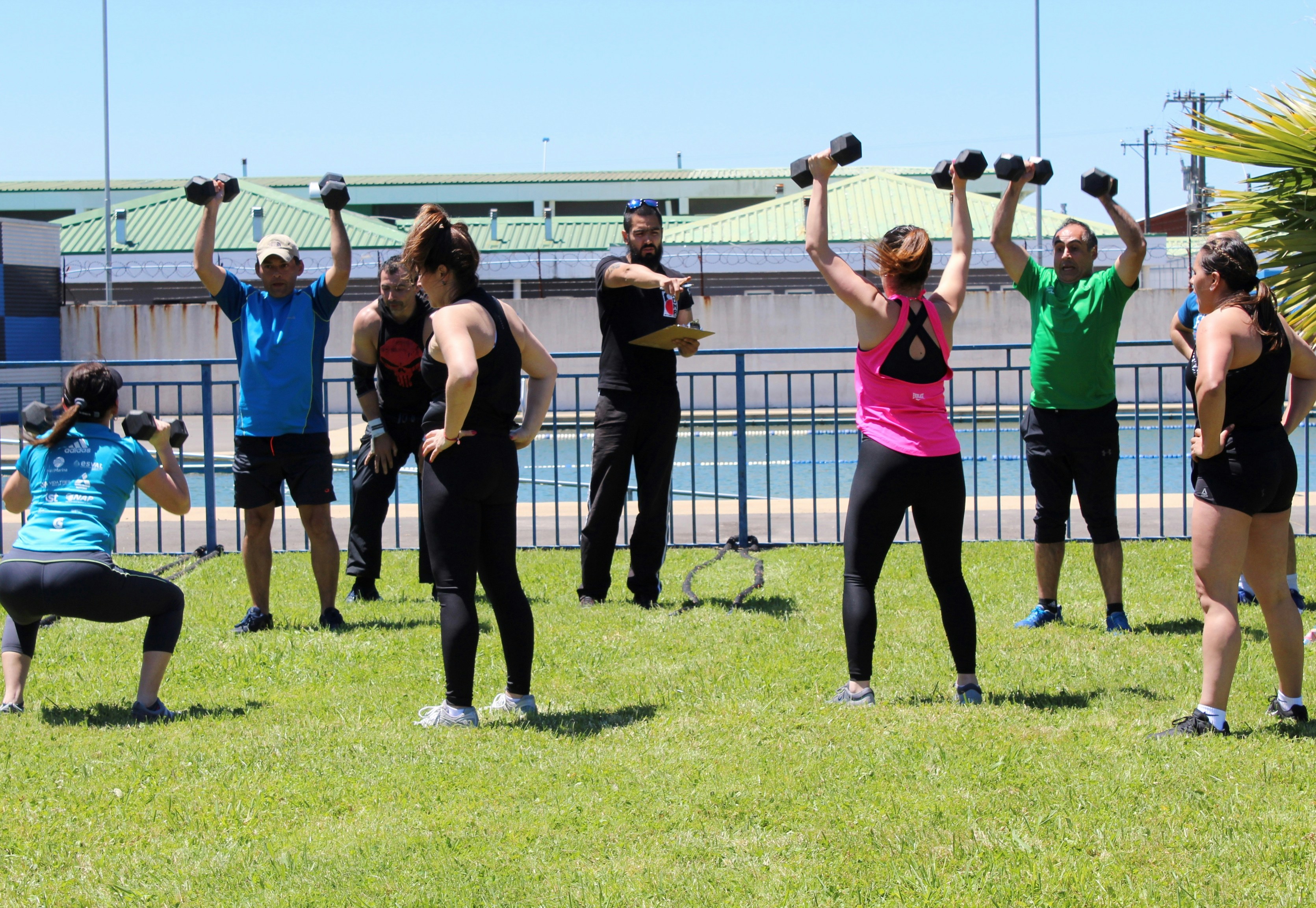 A group of people exercising with dumbbells on a grassy field outdoors.