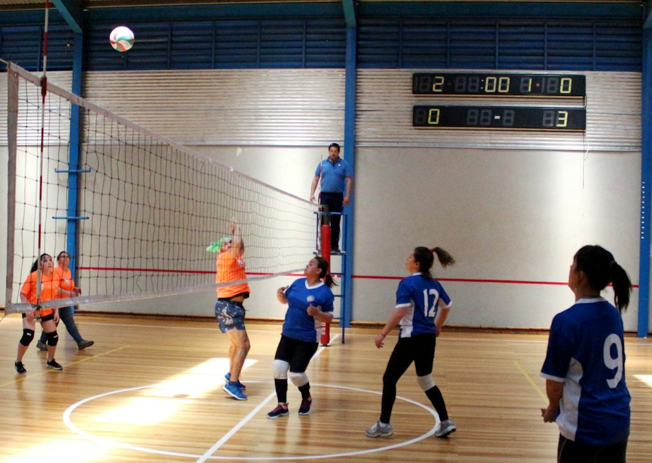 Indoor volleyball match in progress with players competing on a wooden court