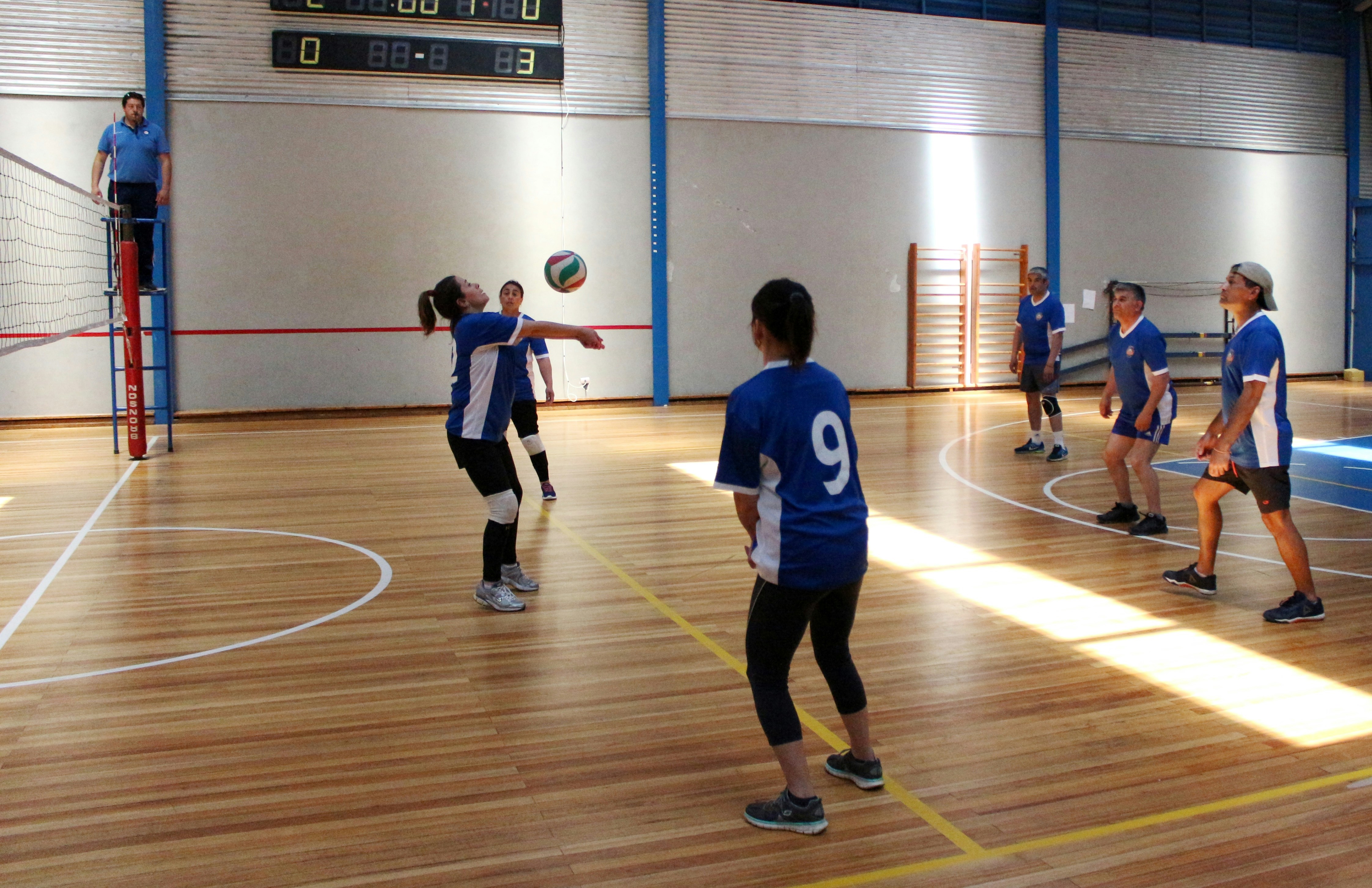 A group of people playing a volleyball match on an indoor wooden court