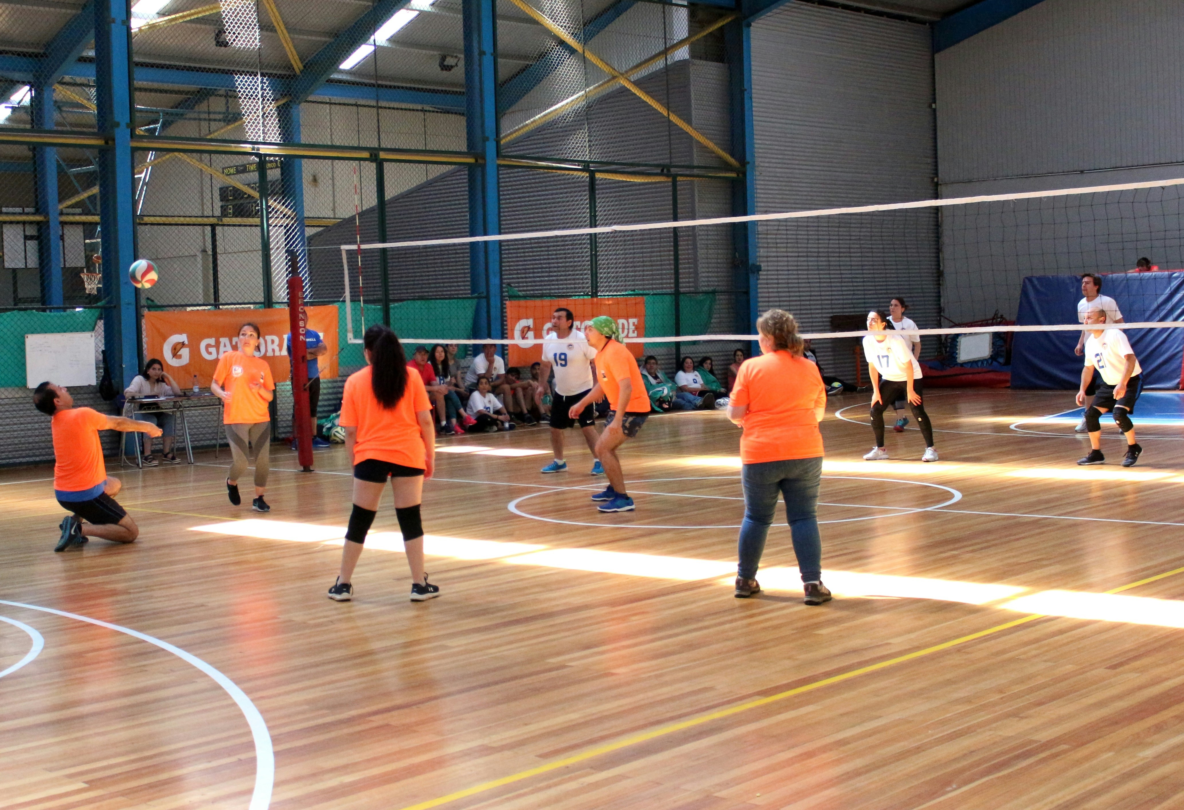 A group of people playing volleyball on an indoor wooden court