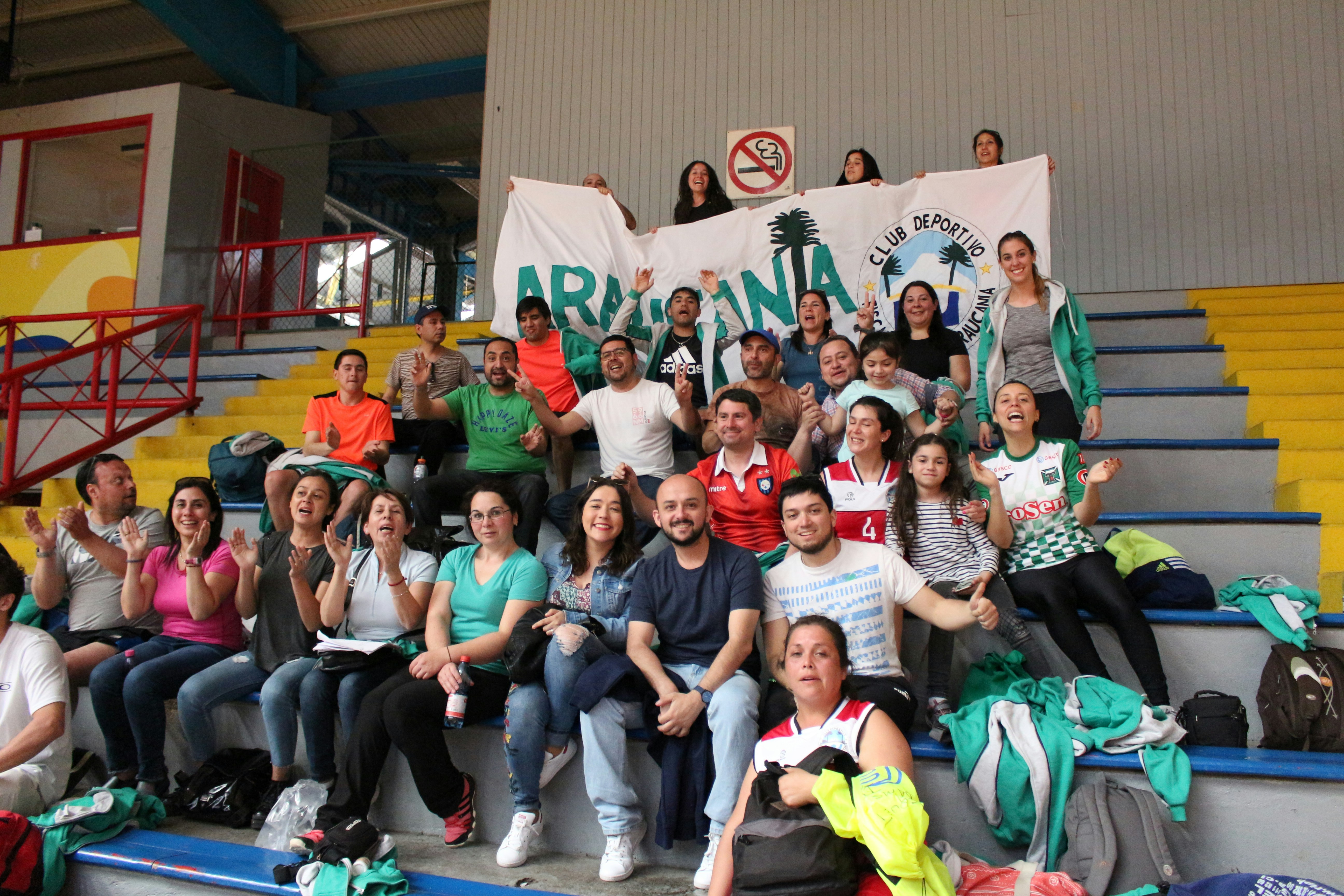 A group of people cheering on stadium bleachers while holding a large banner.