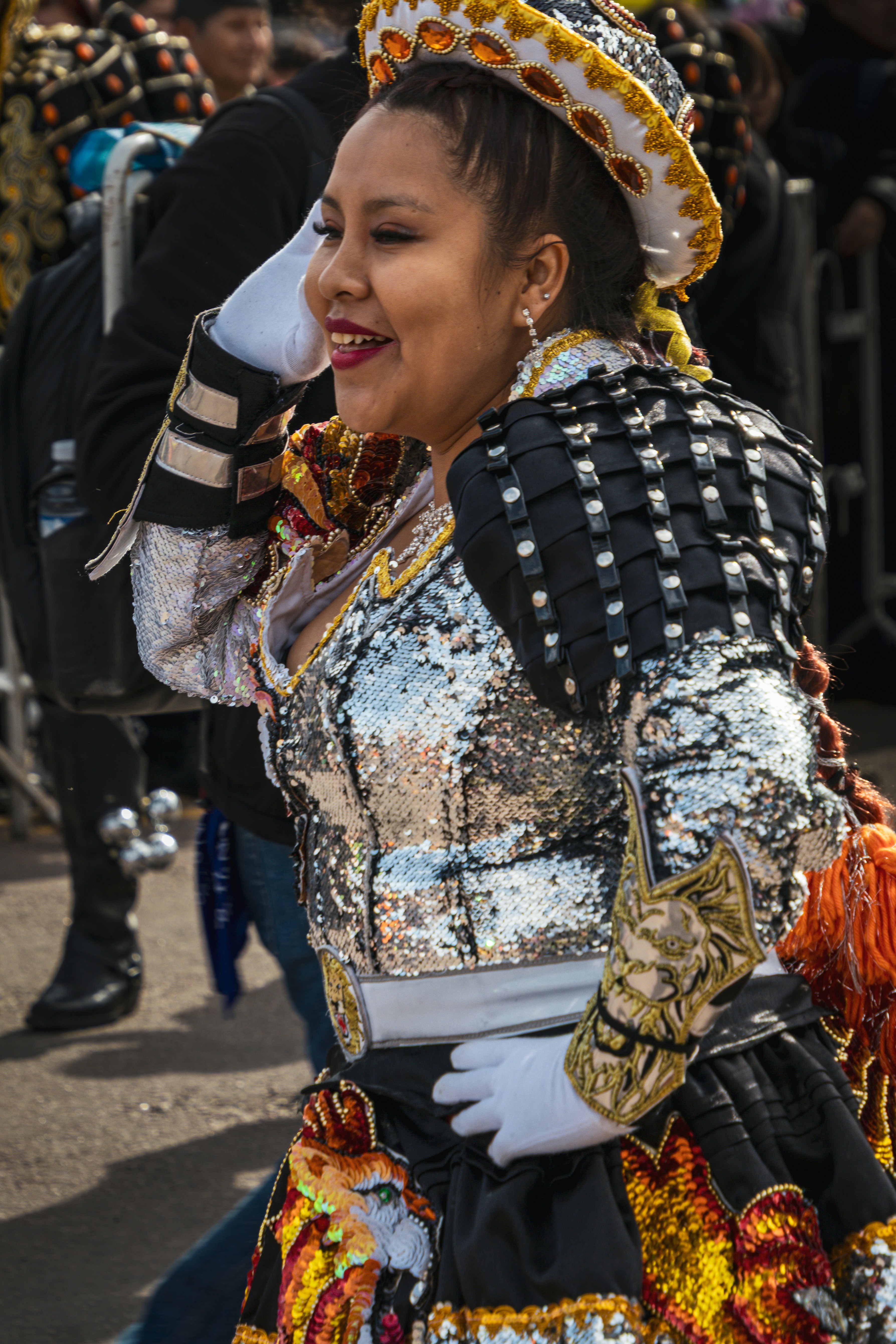 Uma mulher com um traje de lantejoulas e chapéu ornamentado se apresentando em um desfile de rua.