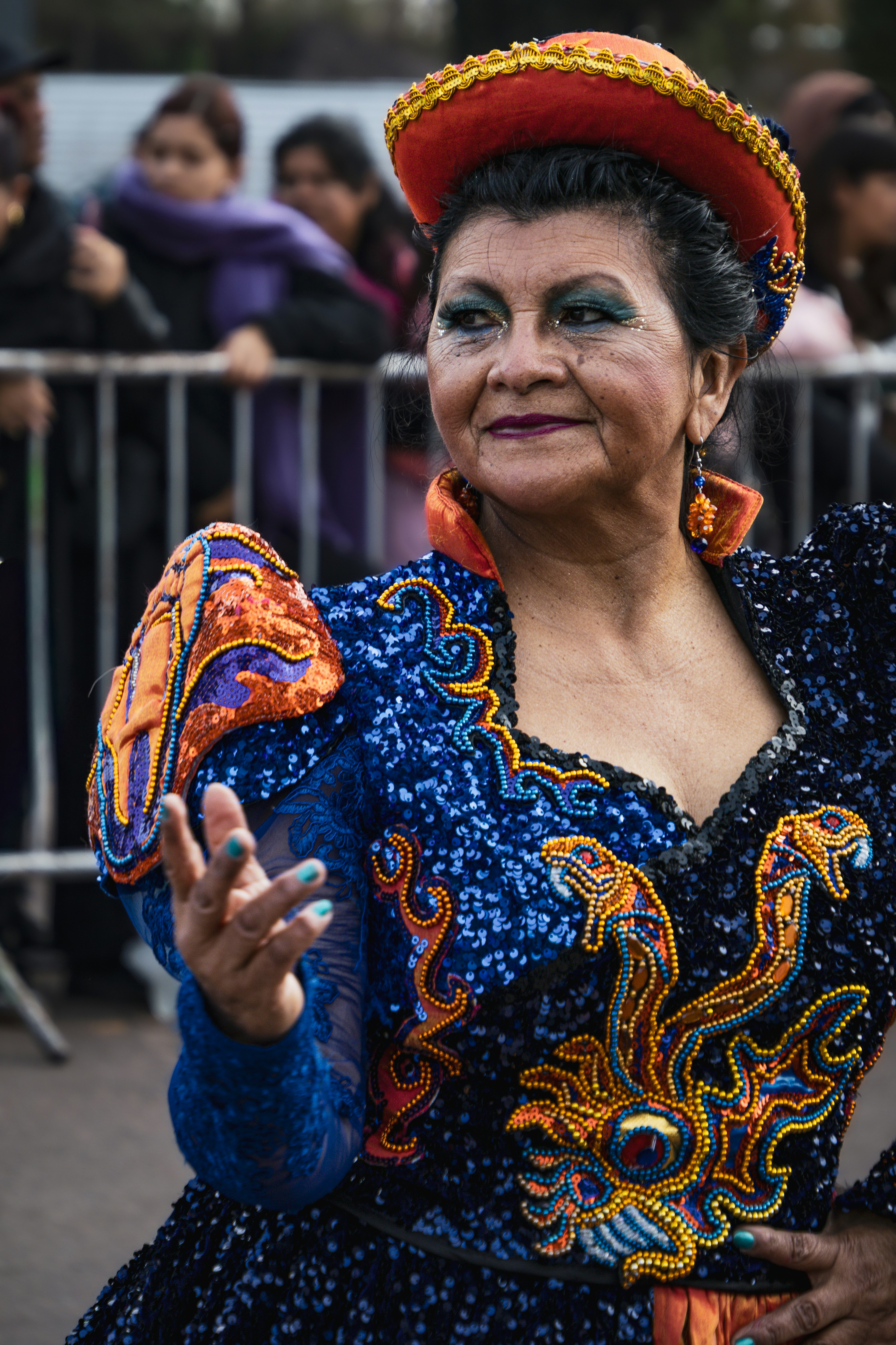 Uma mulher com um traje azul de lantejoulas e chapéu laranja dançando em um desfile.