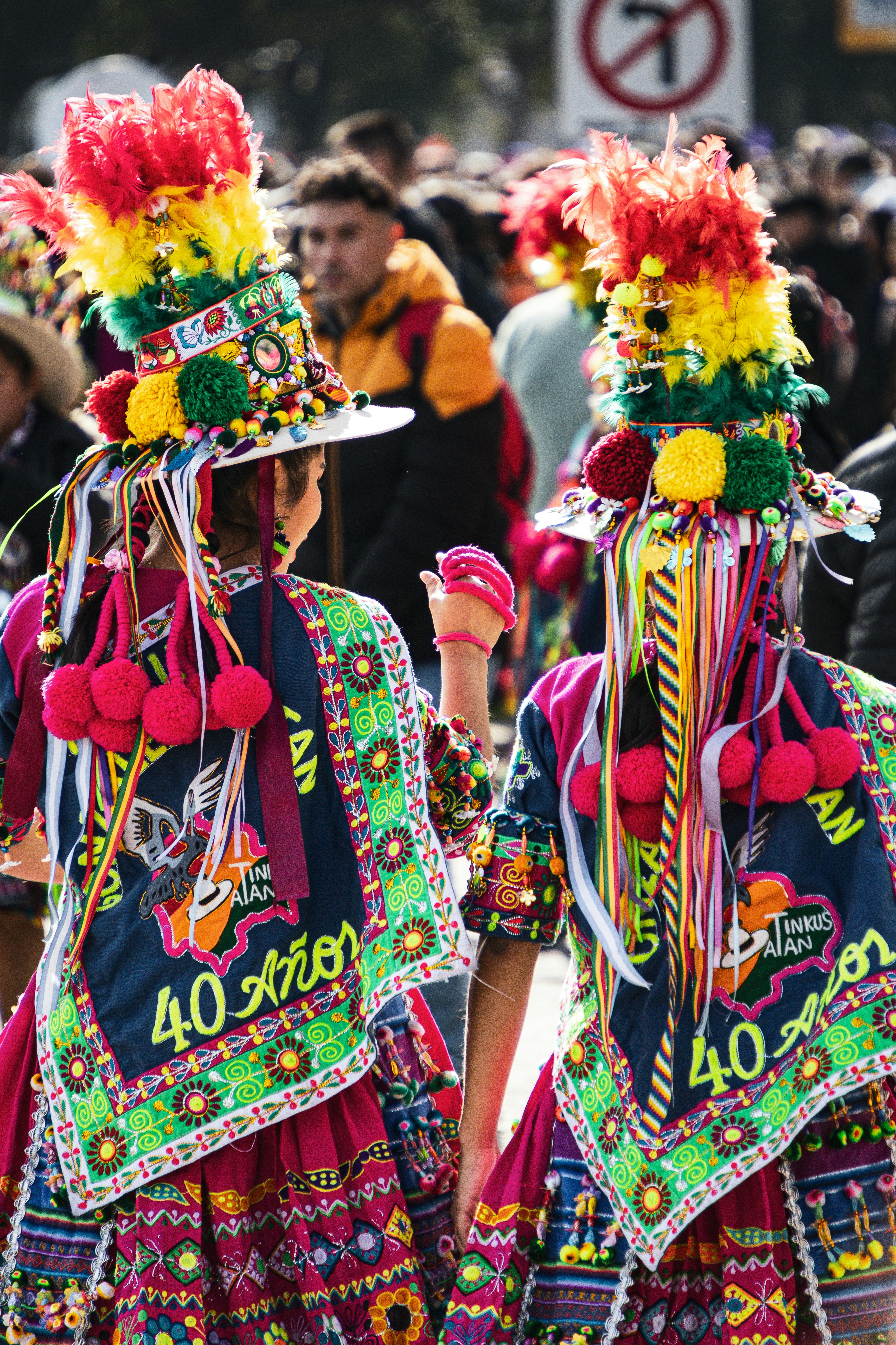 Duas pessoas com trajes tradicionais coloridos e chapéus de penas em um festival de rua.